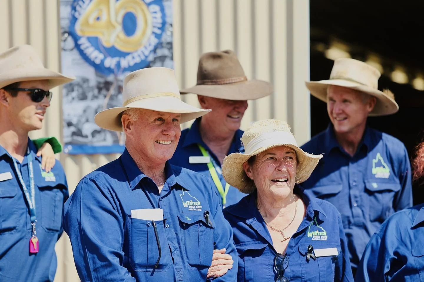 Group of five people wearing blue uniforms and wide-brimmed hats standing outdoors, smiling and looking in different directions.