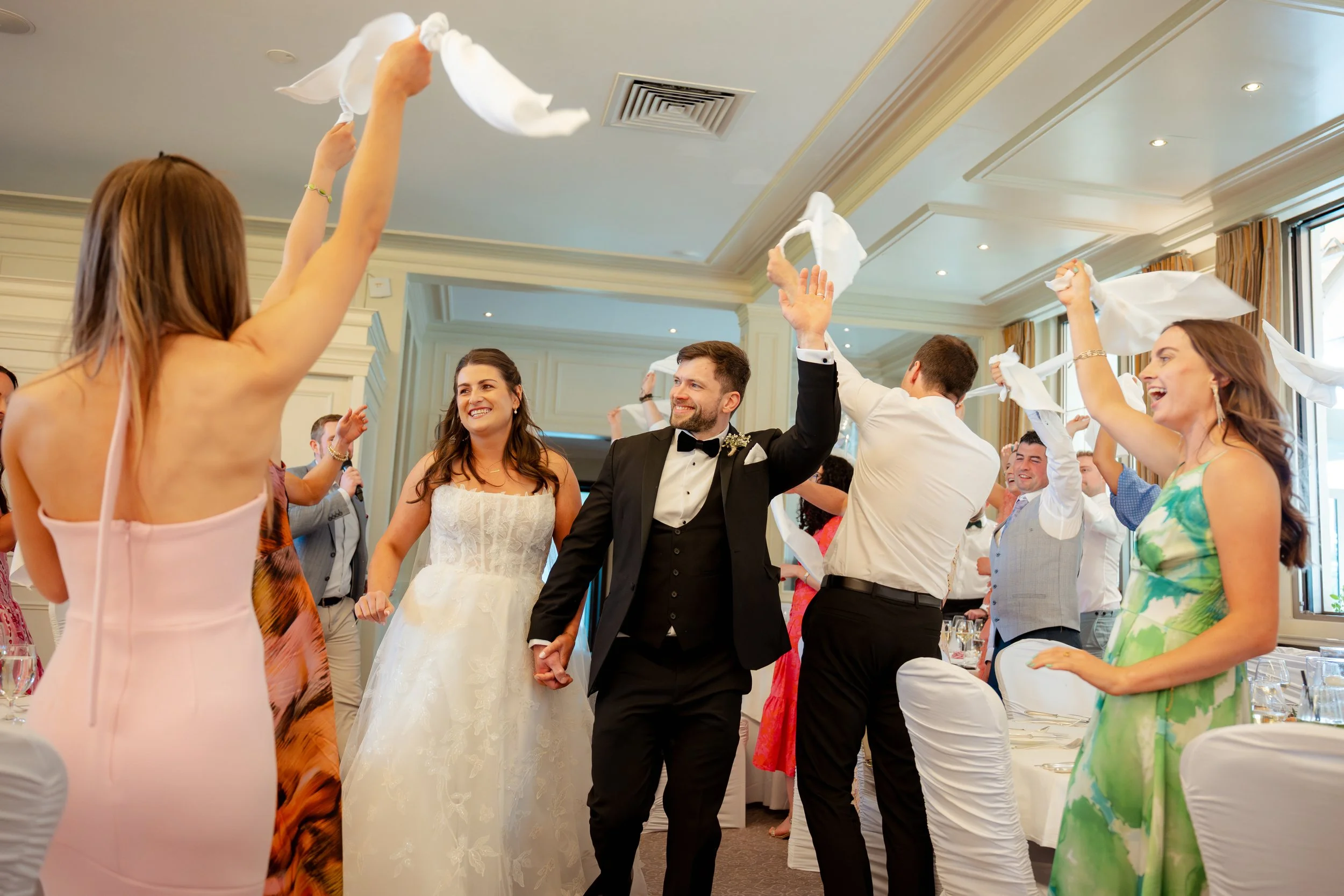 A wedding reception where the bride and groom are dancing together, surrounded by guests celebrating and waving napkins.