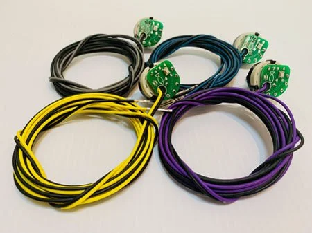 Four bundles of multicolored wires with small green circuit boards attached, arranged on a white surface.