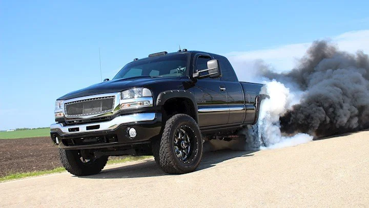 A black pickup truck driving on a road with smoke and dust billowing from behind it.