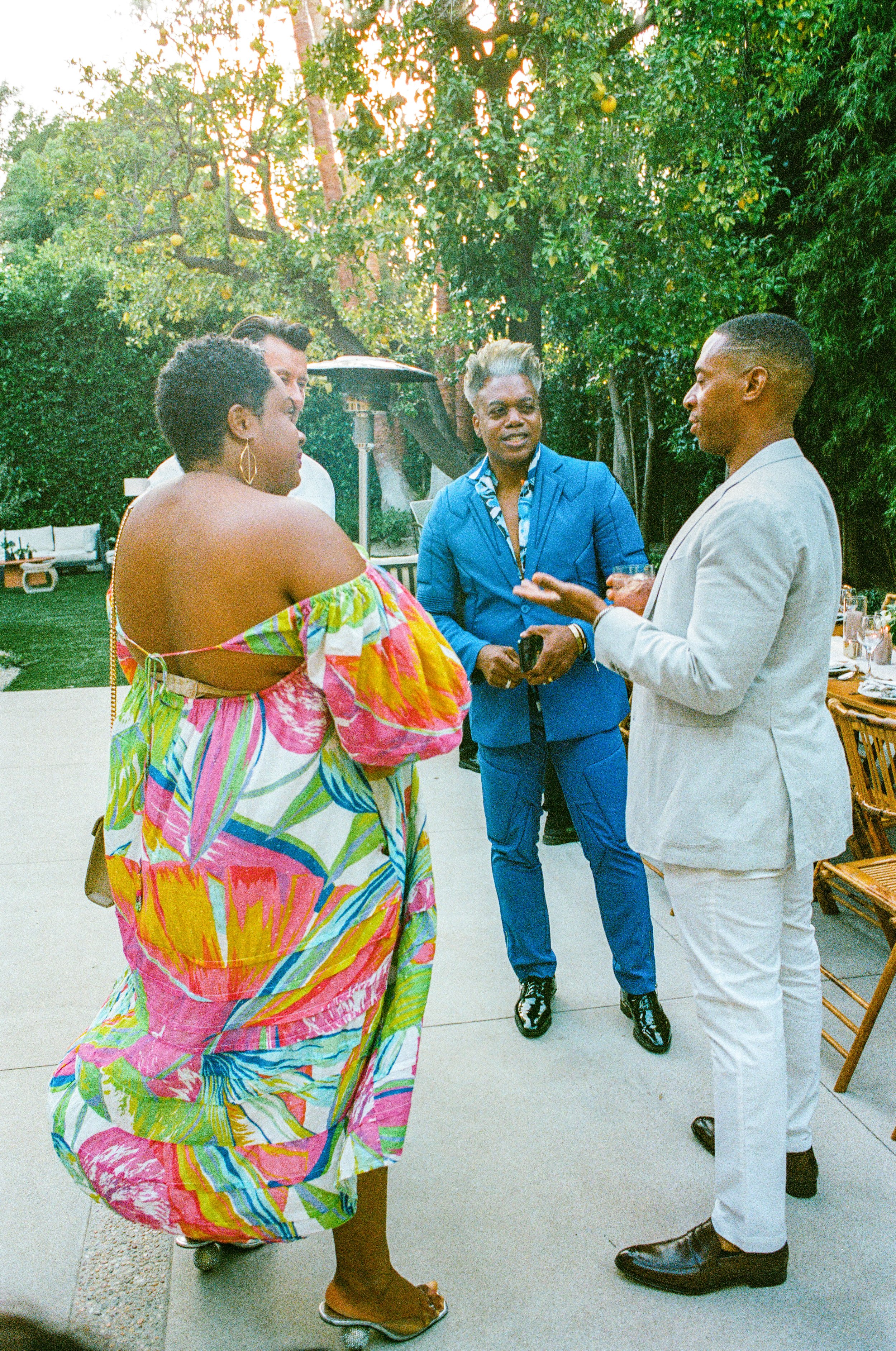 A group of five people talking at an outdoor gathering in a backyard with greenery and patio furniture.