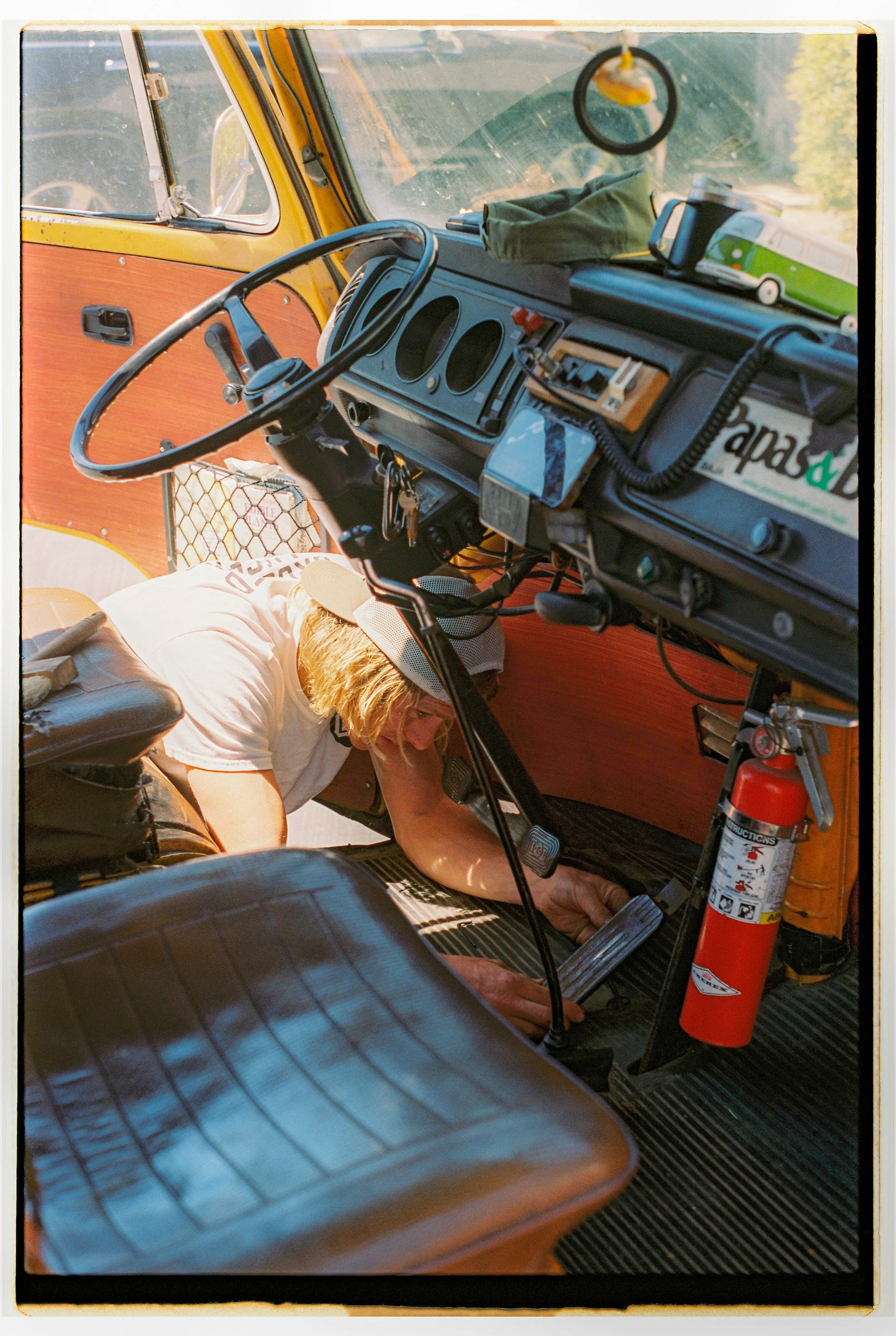 Person working under the dashboard of a vintage yellow vehicle, possibly a camper or bus.