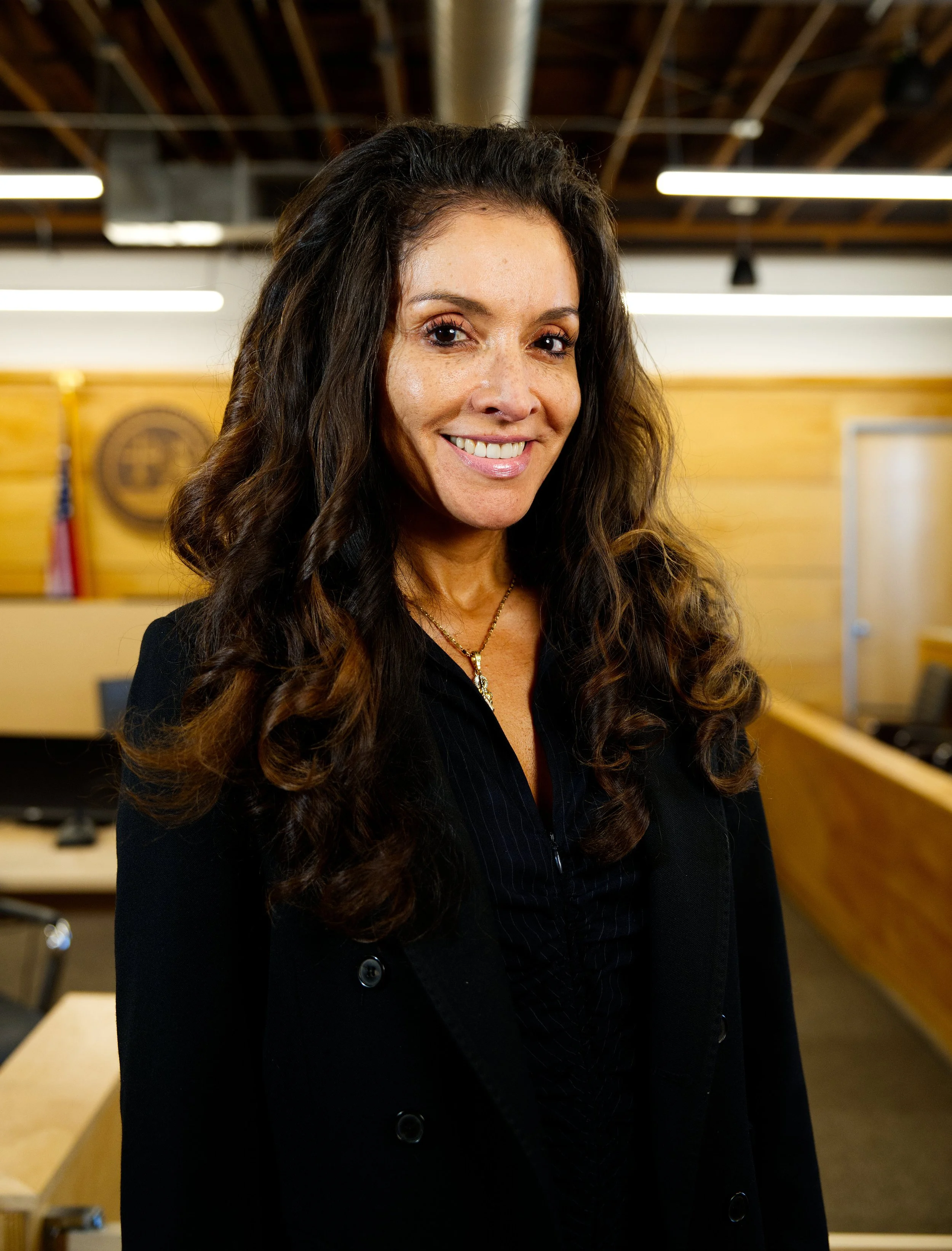 Mujer sonriendo en una oficina con paredes de madera y banderas al fondo.