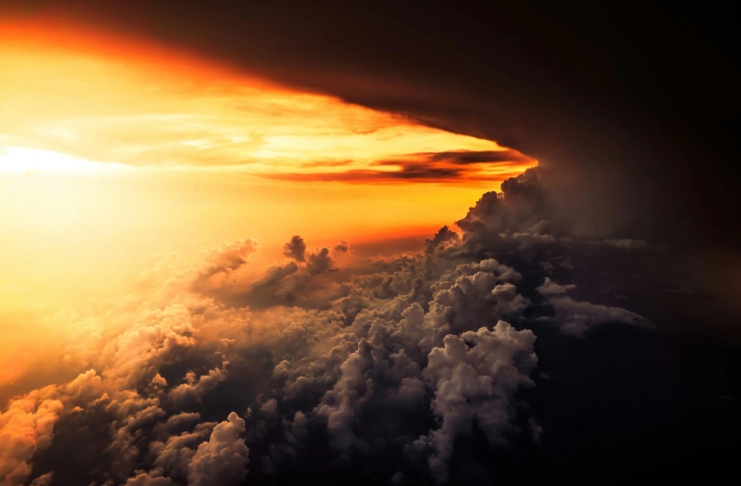 View of clouds from above with a vivid sunset casting orange and yellow hues against dark clouds.