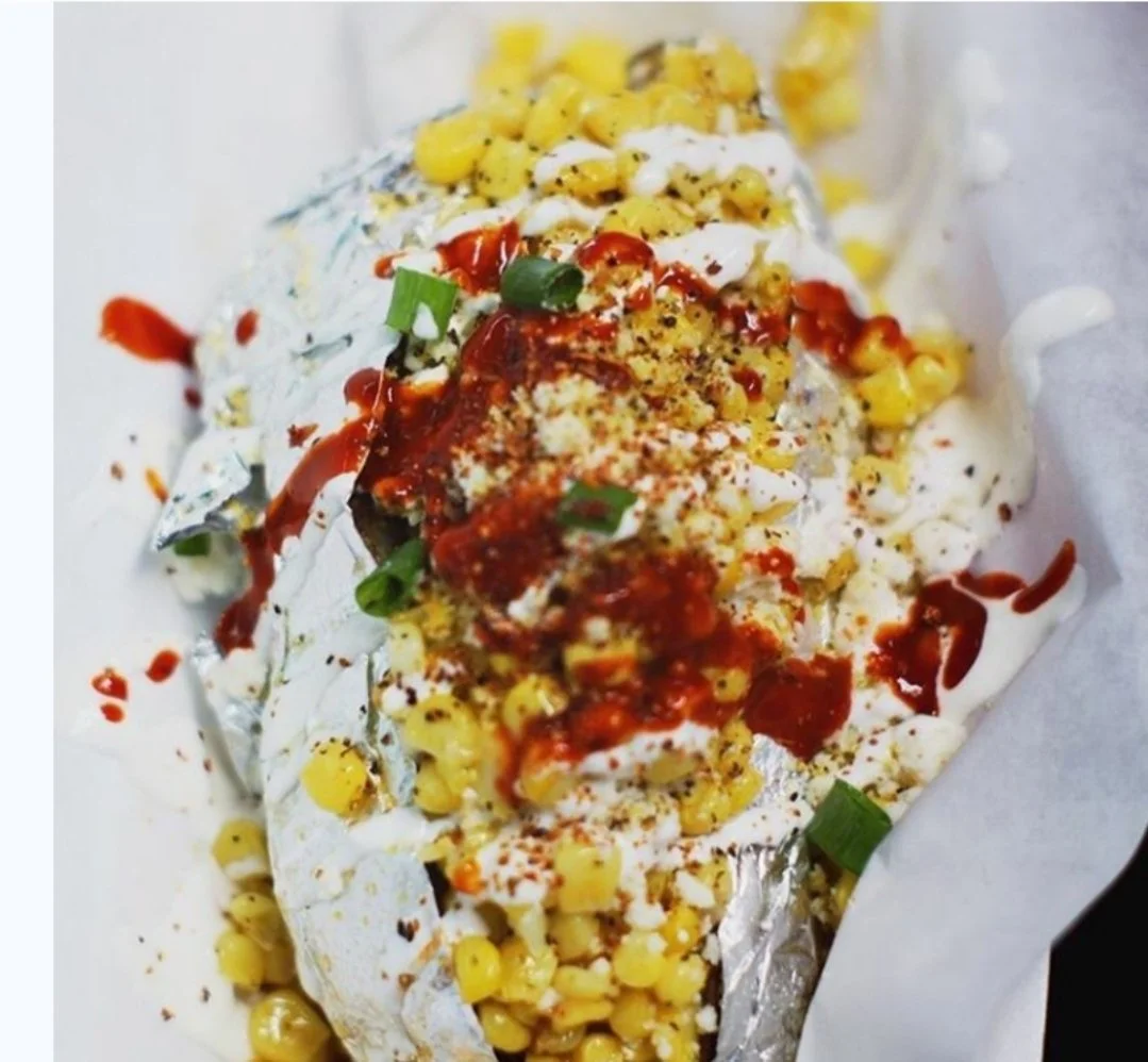 Close-up of a baked fish topped with corn, green onions, red sauce, and spices, resting on foil with parchment paper.