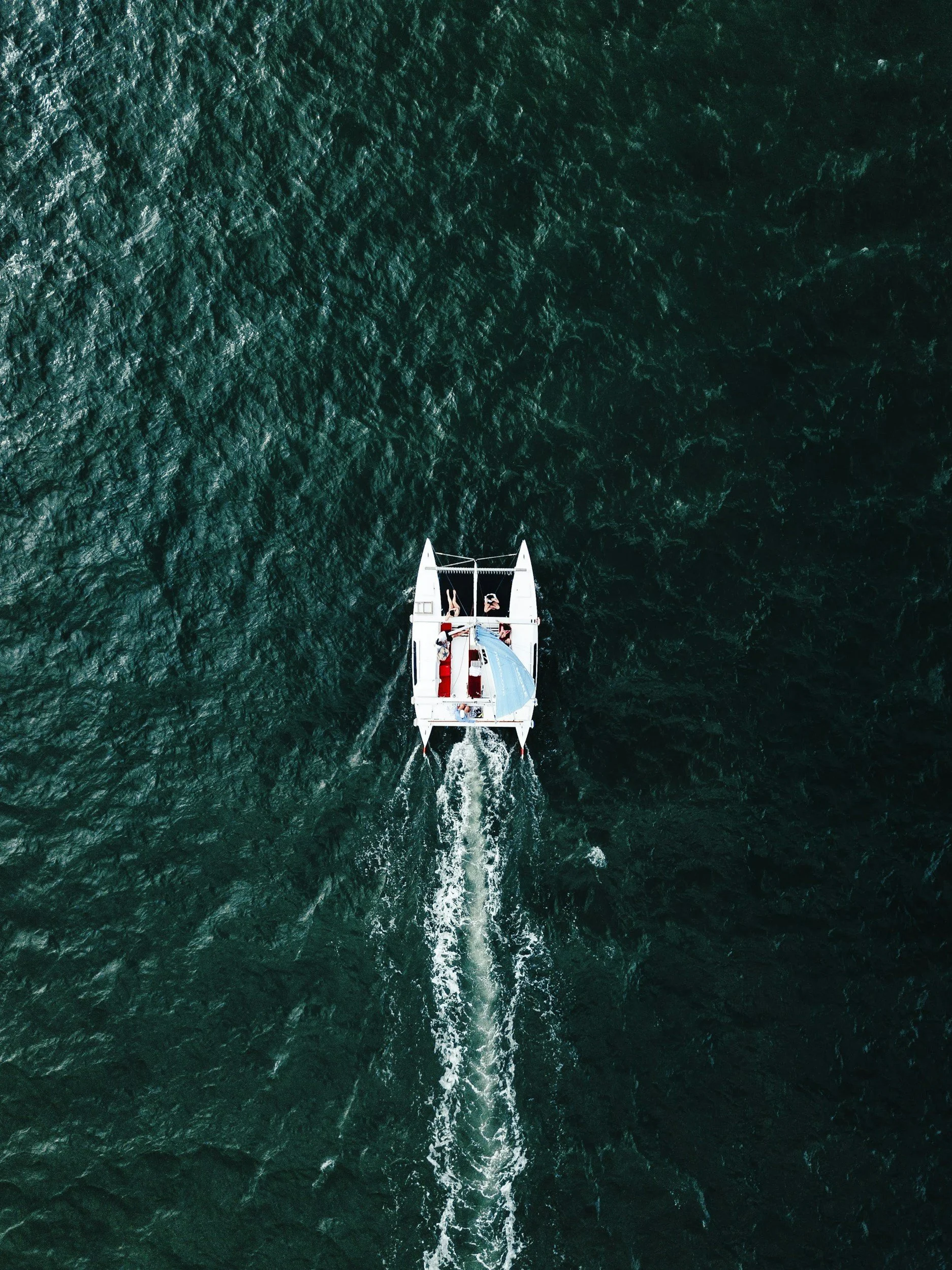 Aerial view of a white boat with red accents cruising through dark green water, leaving a white wake behind.