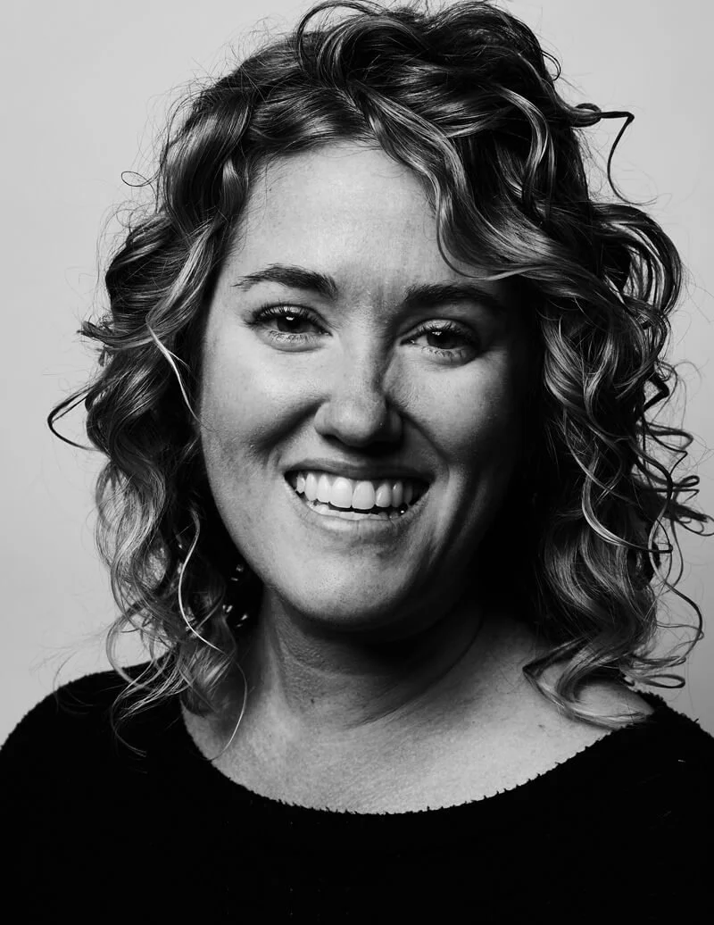Black and white portrait of a woman with curly hair smiling at the camera.