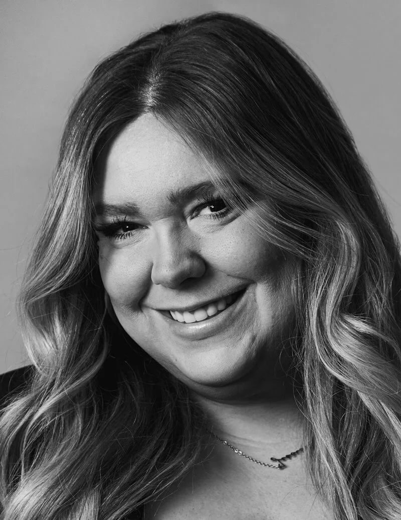 Black and white portrait of a woman with long, wavy hair, smiling and looking at the camera.