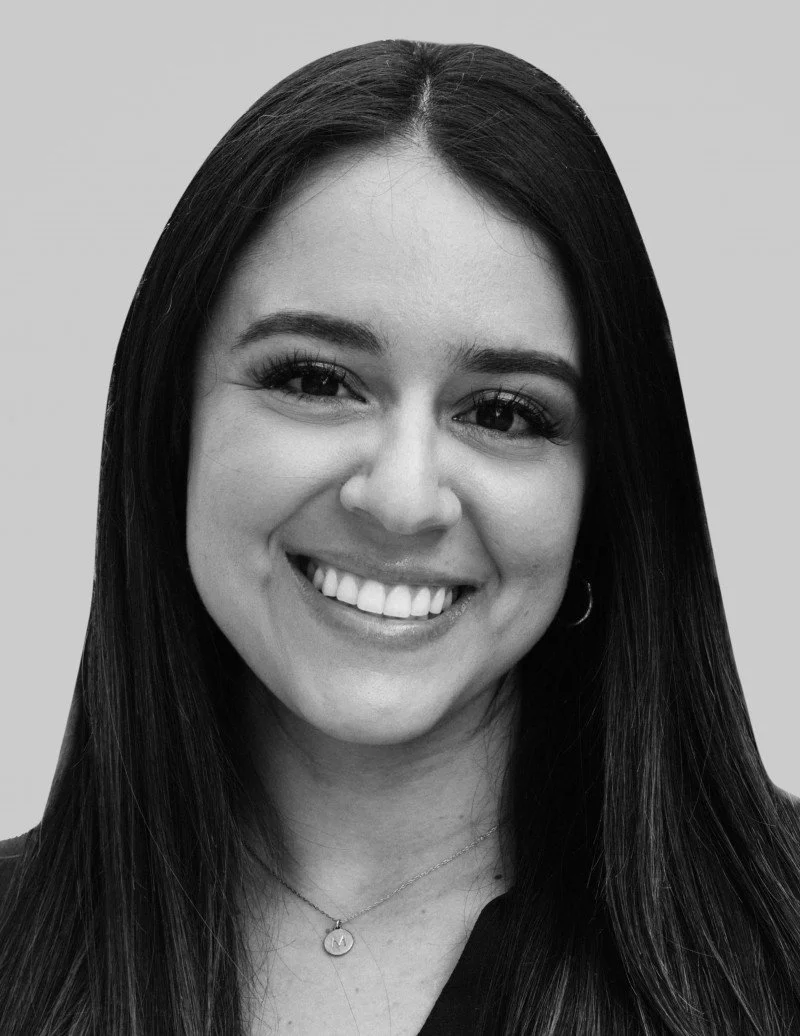 Black-and-white photo of a woman with long dark hair, smiling, wearing earrings and a necklace.