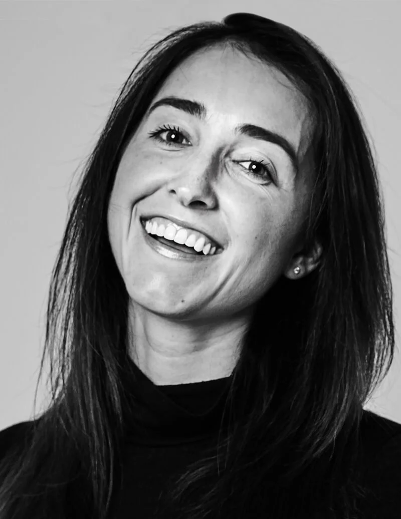 A woman with long dark hair, smiling broadly, wearing a black turtleneck, in a black and white photo.