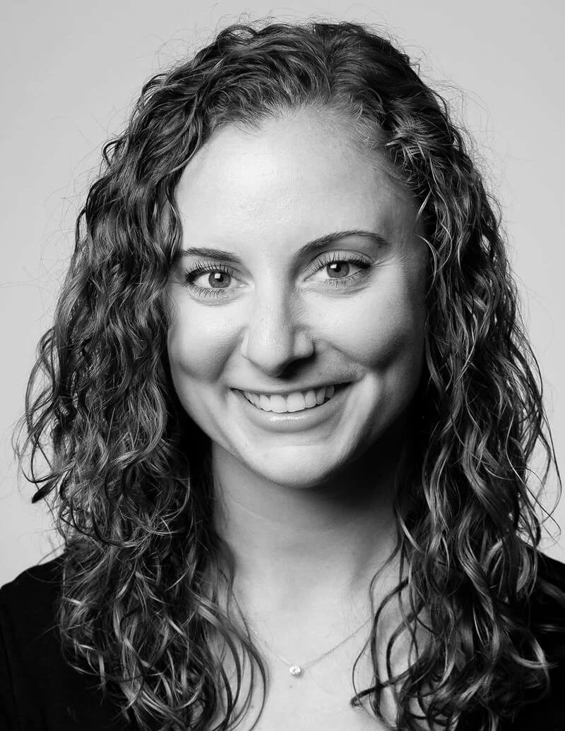 Black and white portrait of a young woman with curly hair smiling at the camera.