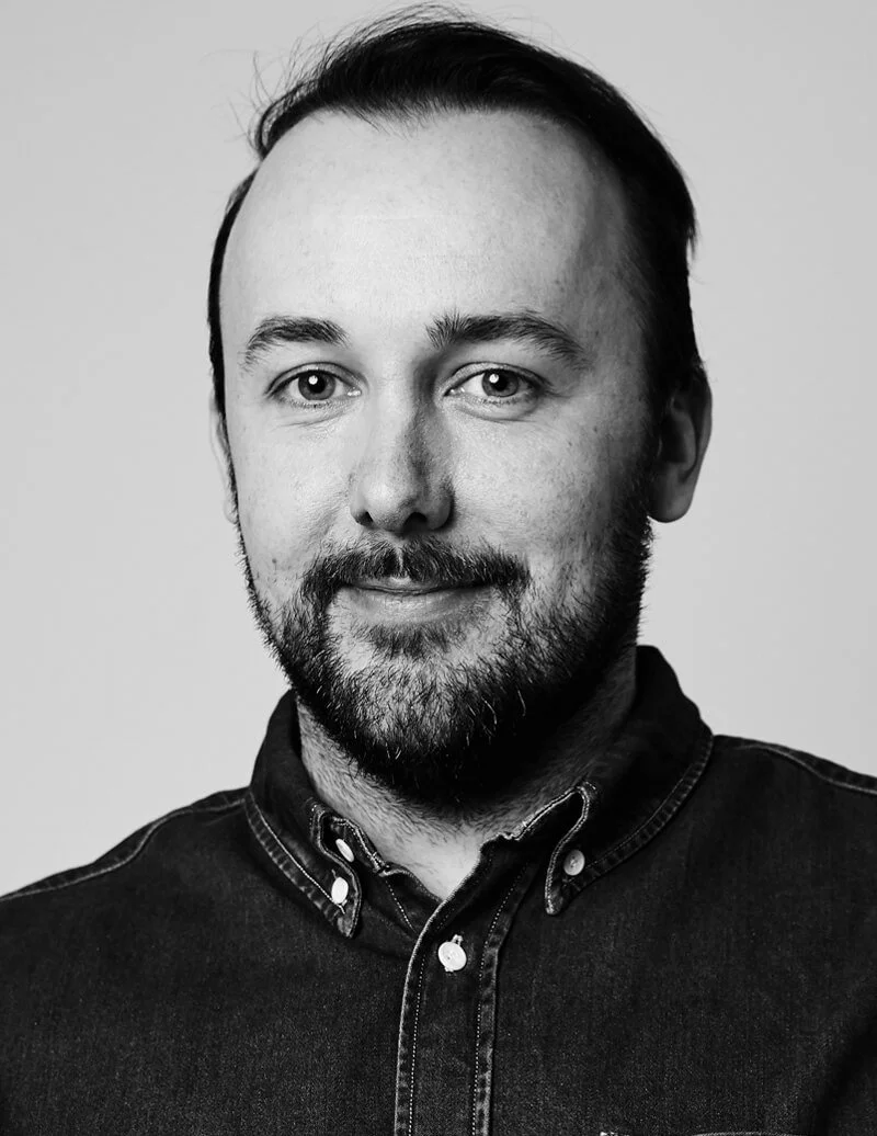 Black and white portrait of a man with a beard, short hair, wearing a button-up shirt, smiling slightly.