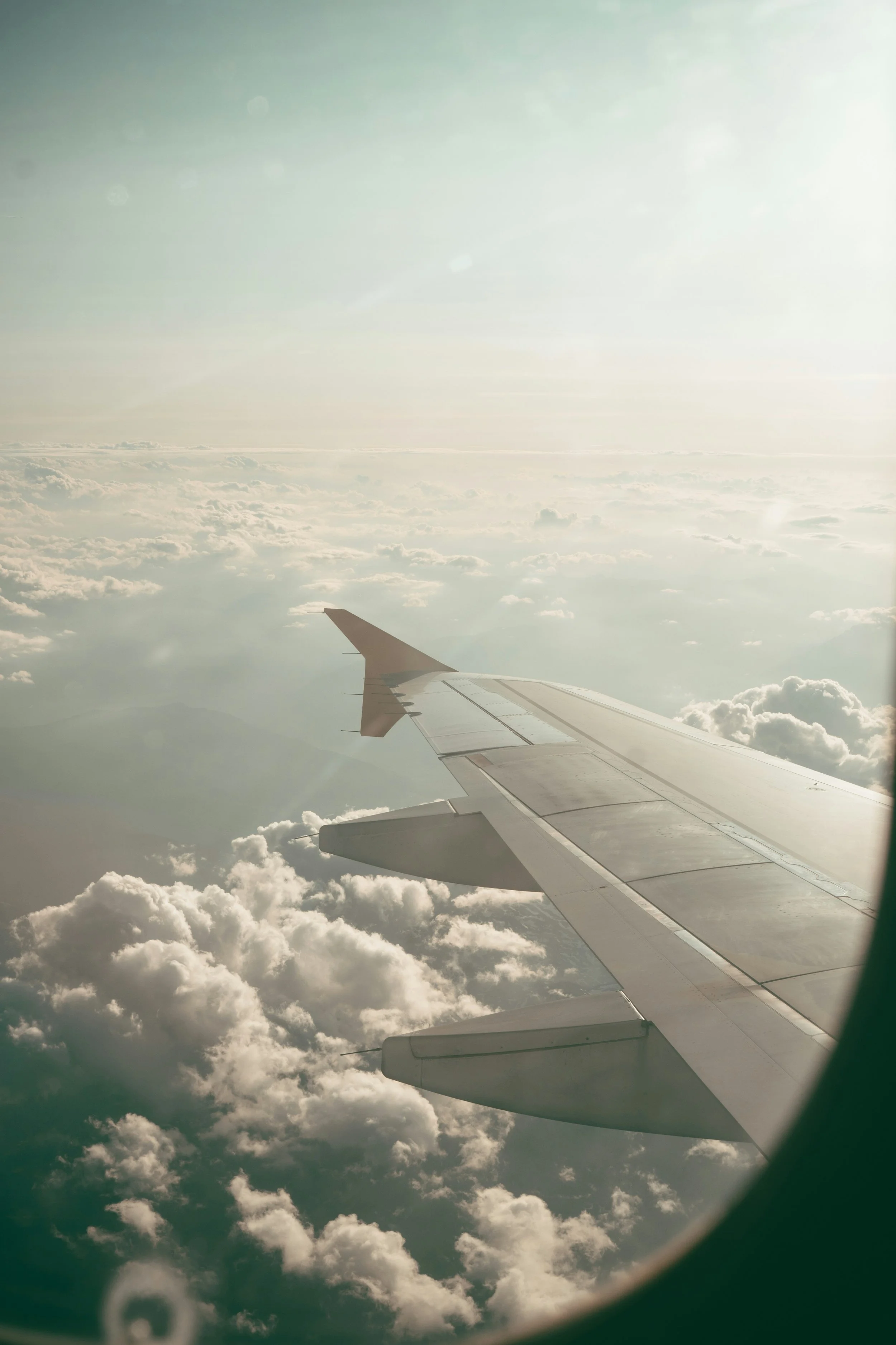 View from an airplane window showing the plane wing and a cloudy sky outside.