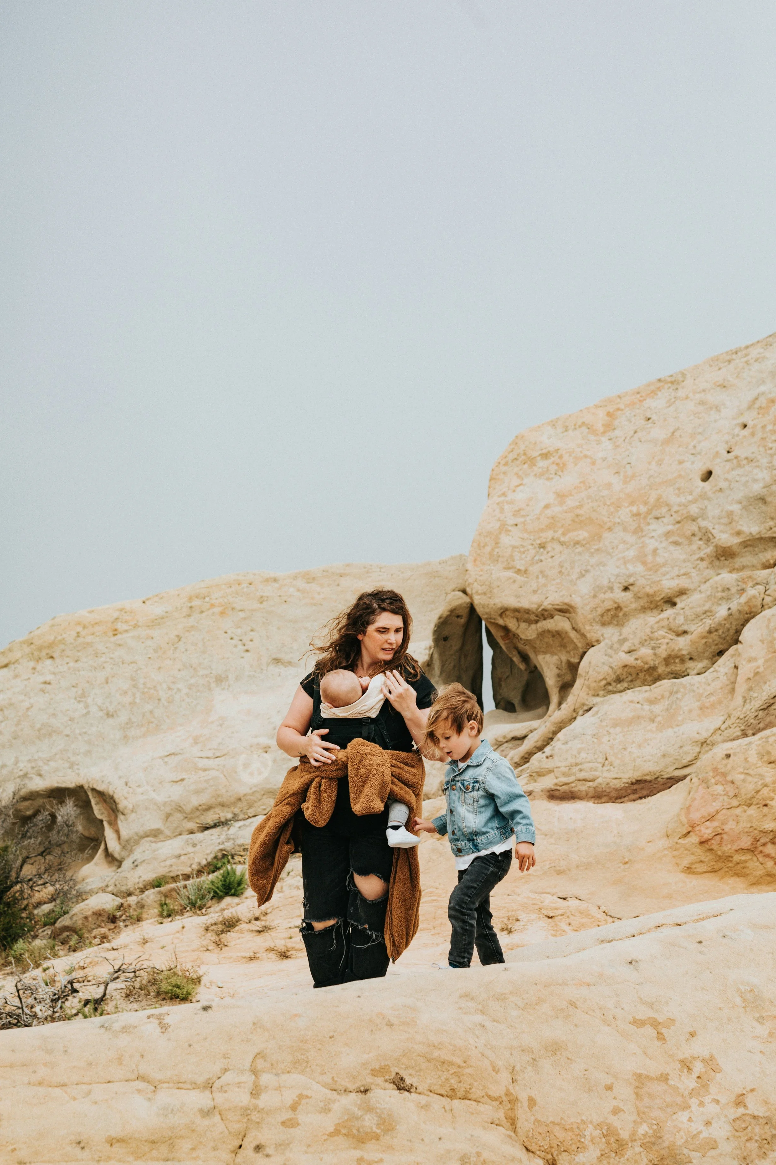A woman holding a baby and a young boy walking among large rock formations in a desert landscape.