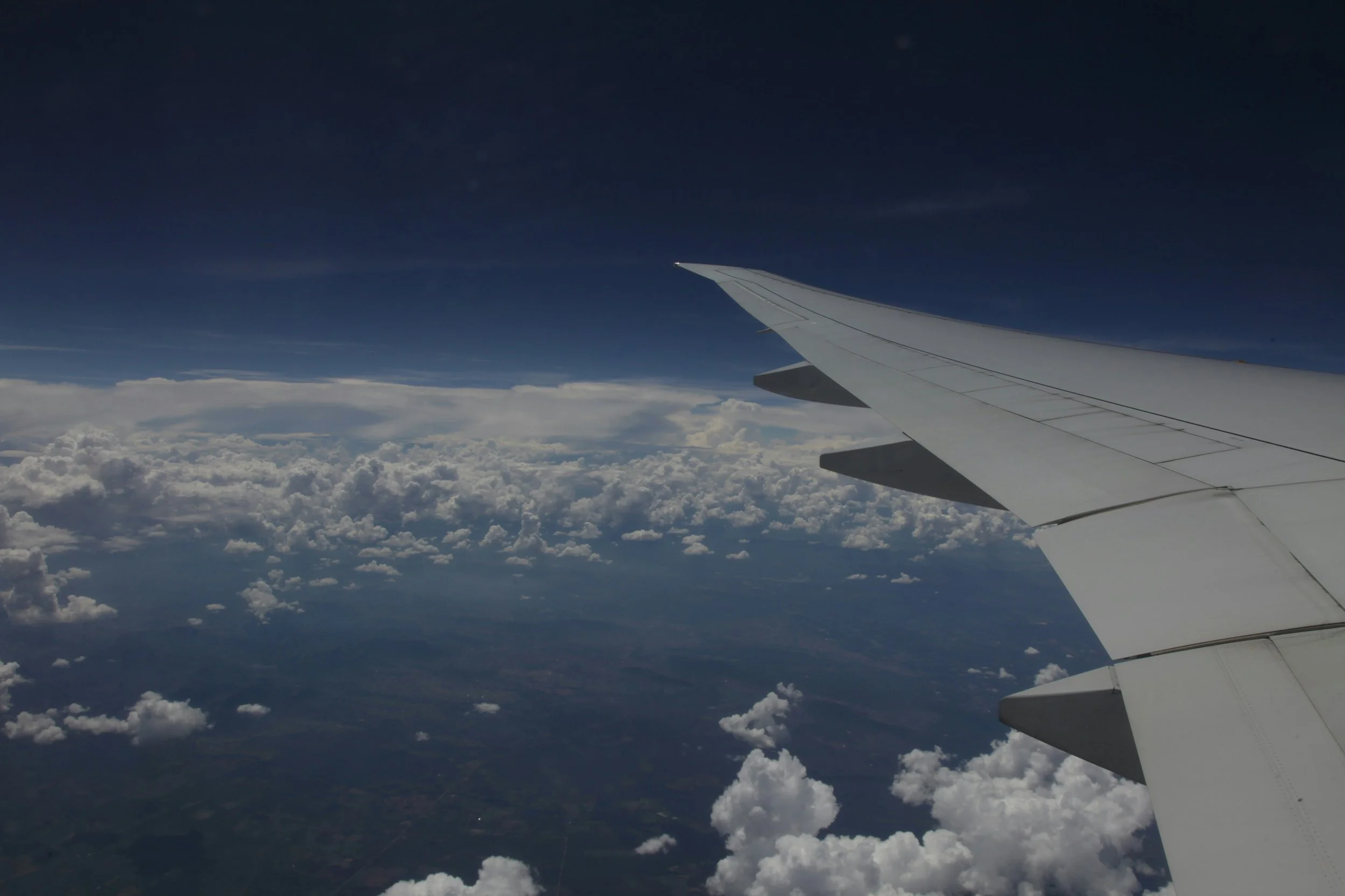 View from an airplane window showing the wing with a cloudy sky and layers of clouds below.