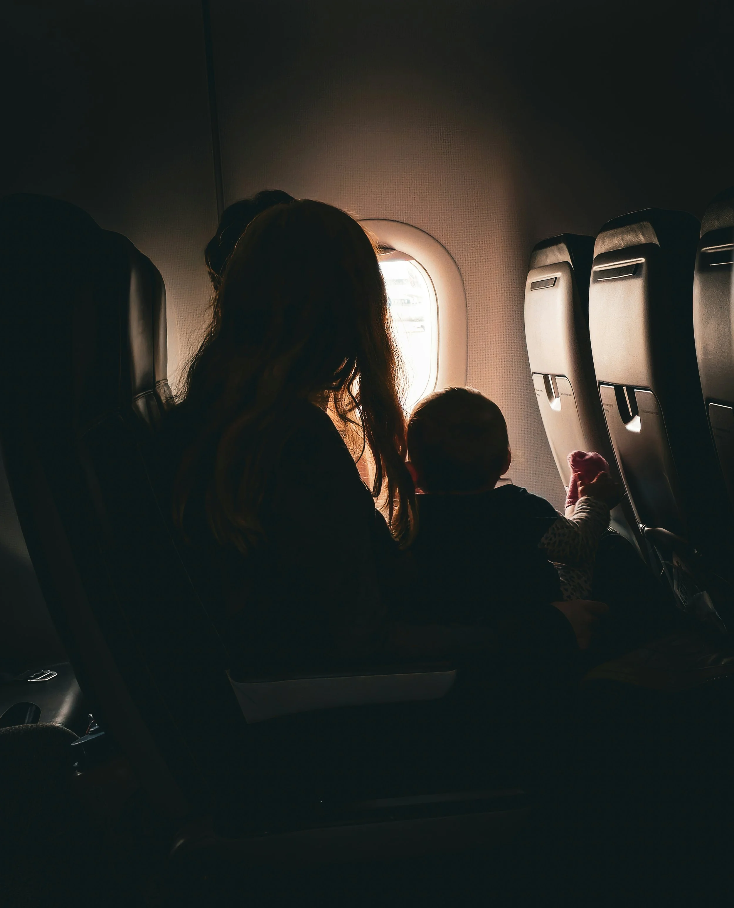 Passenger sitting on airplane window seat during daytime, with sunlight streaming through the window.