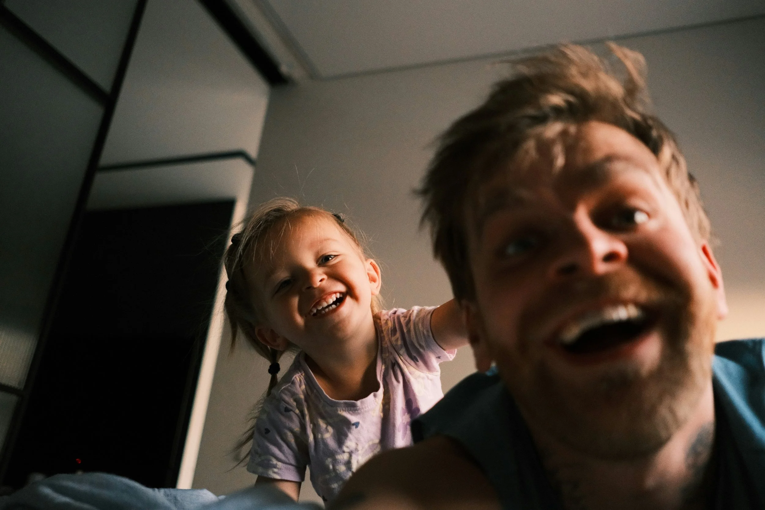 A close-up of a young man and a young girl playing peekaboo, smiling and laughing at each other indoors.