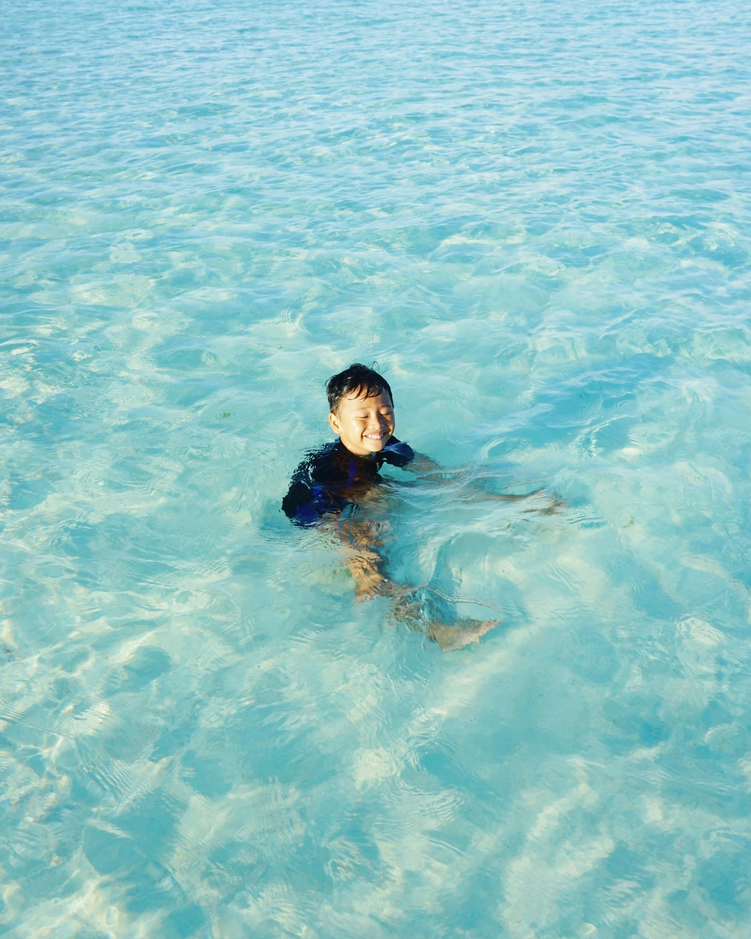A young boy with wet hair smiling and enjoying himself in a swimming pool, surrounded by clear blue water.