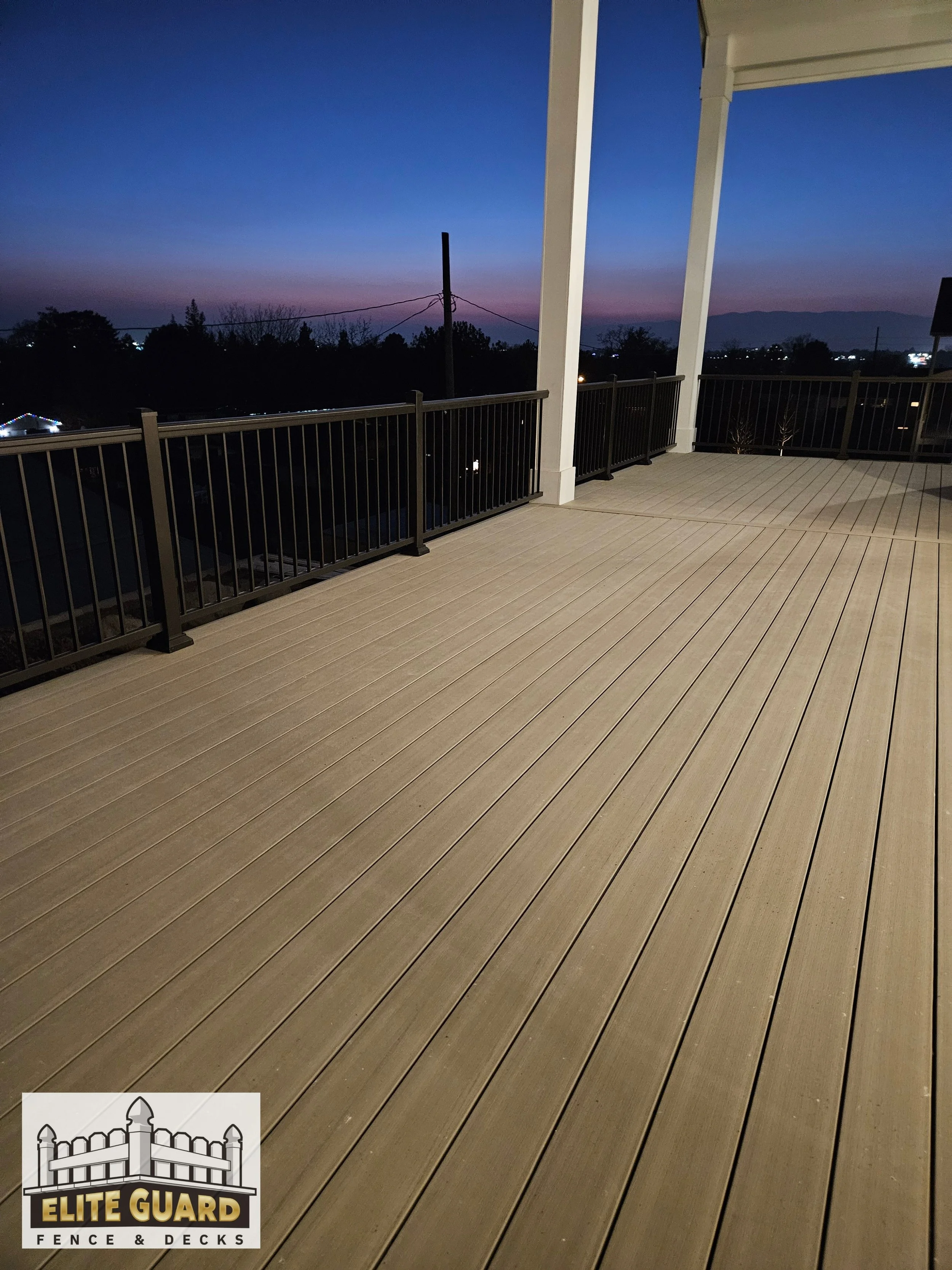 Empty outdoor deck with beige boards and black railing, overlooking a landscape during dusk with a darkening sky and distant mountains in Spanish Fork, Utah.