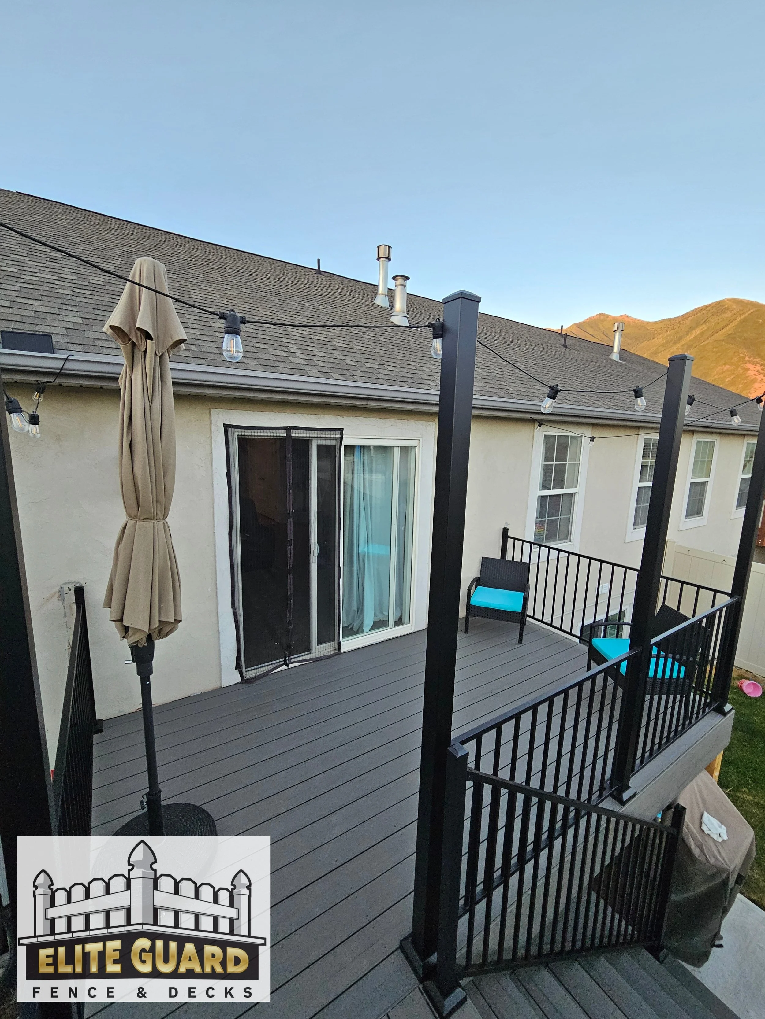 Backyard deck with seating, string lights, umbrella, sliding glass door, and mountain view at sunset in Salem, Utah.