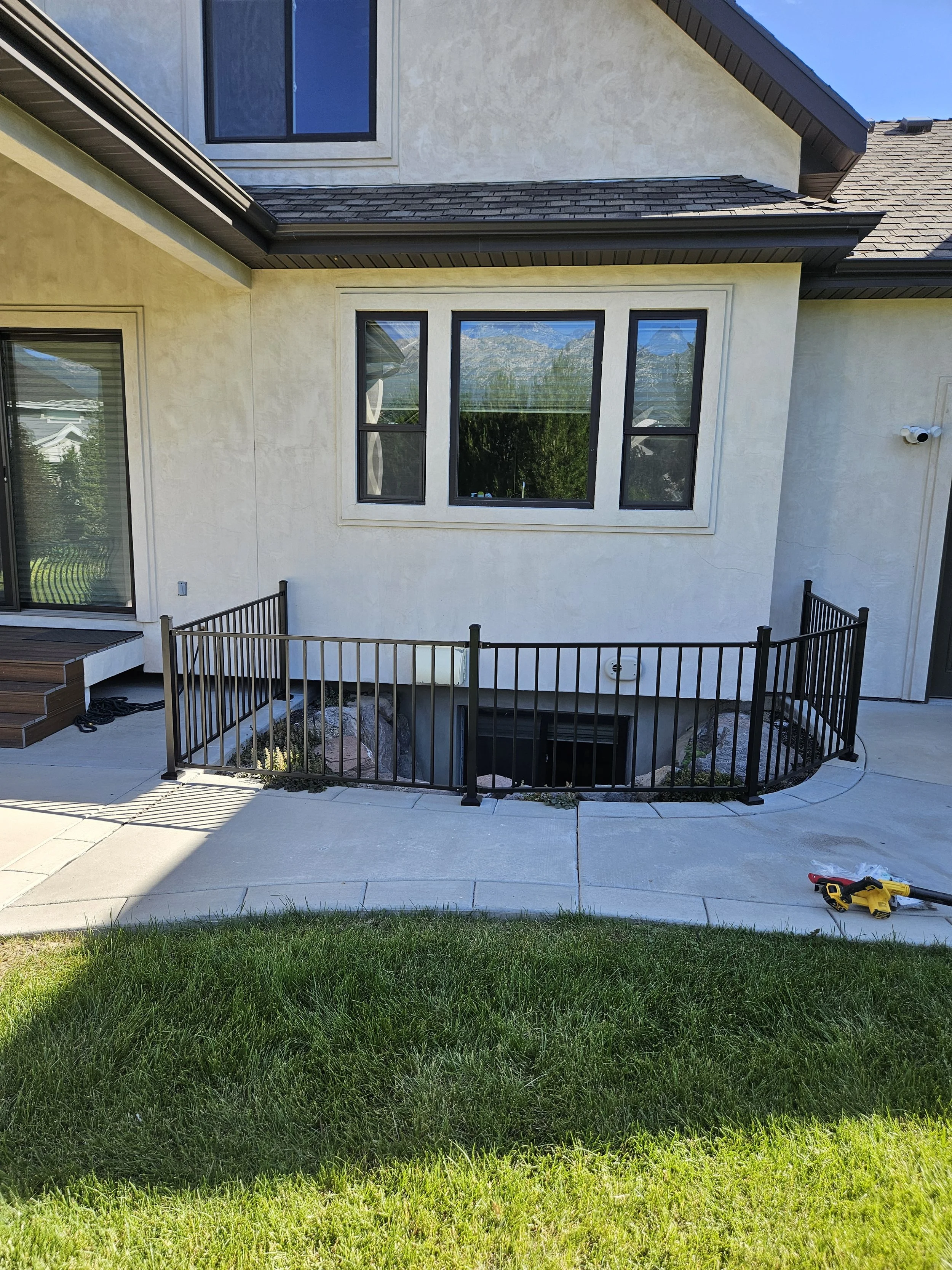 Backyard view of a house with a small fenced patio area, rocks, and plants beneath the window, and a yellow power drill on the concrete patio in Payson, UT.