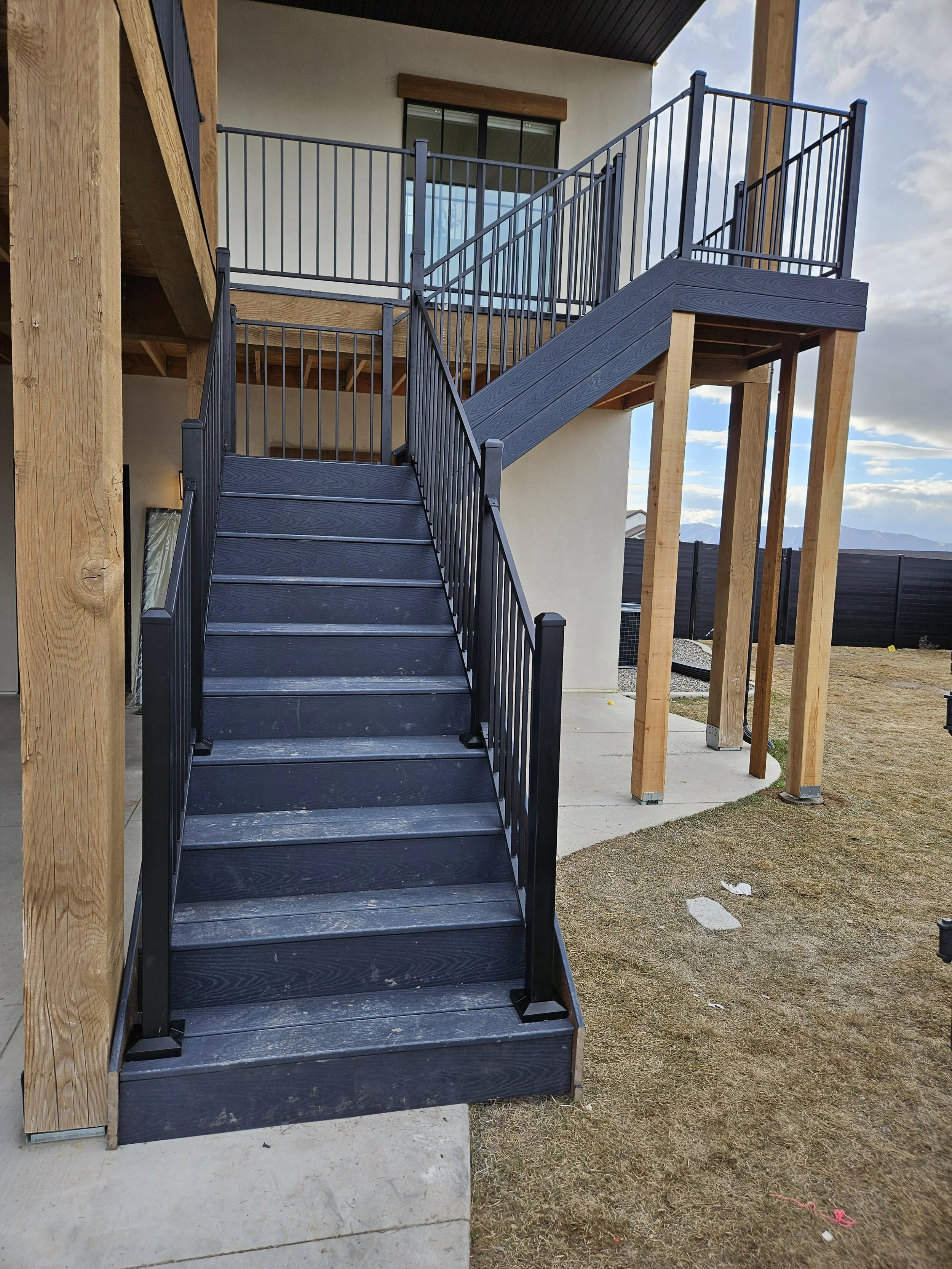 Black outdoor staircase with metal railings leading to an upper balcony of a modern house, with wooden supports and a grassy yard in Payson, UT.
