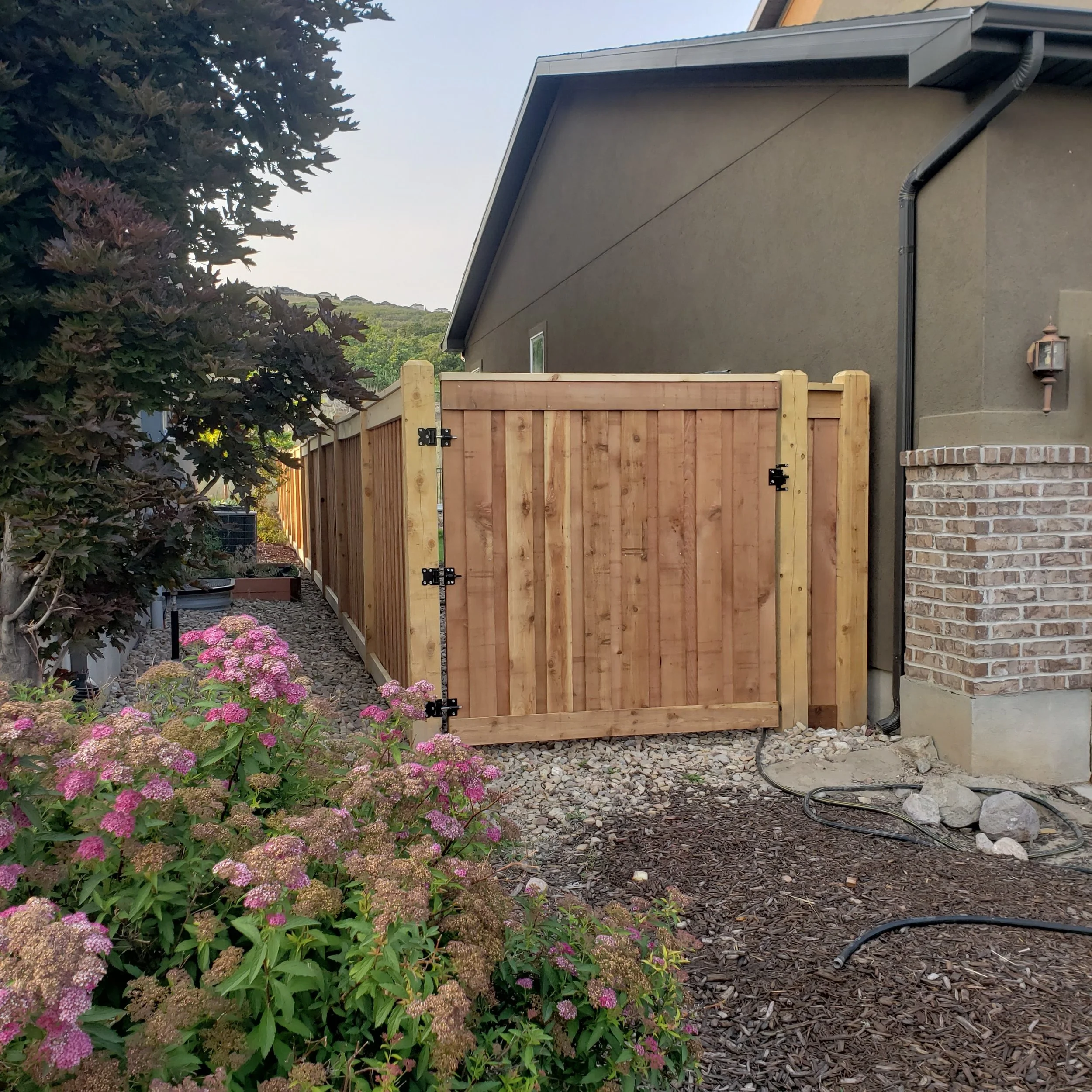 New wooden fence gate installed on side yard of house with plants and flowers in foreground in Payson, UT.