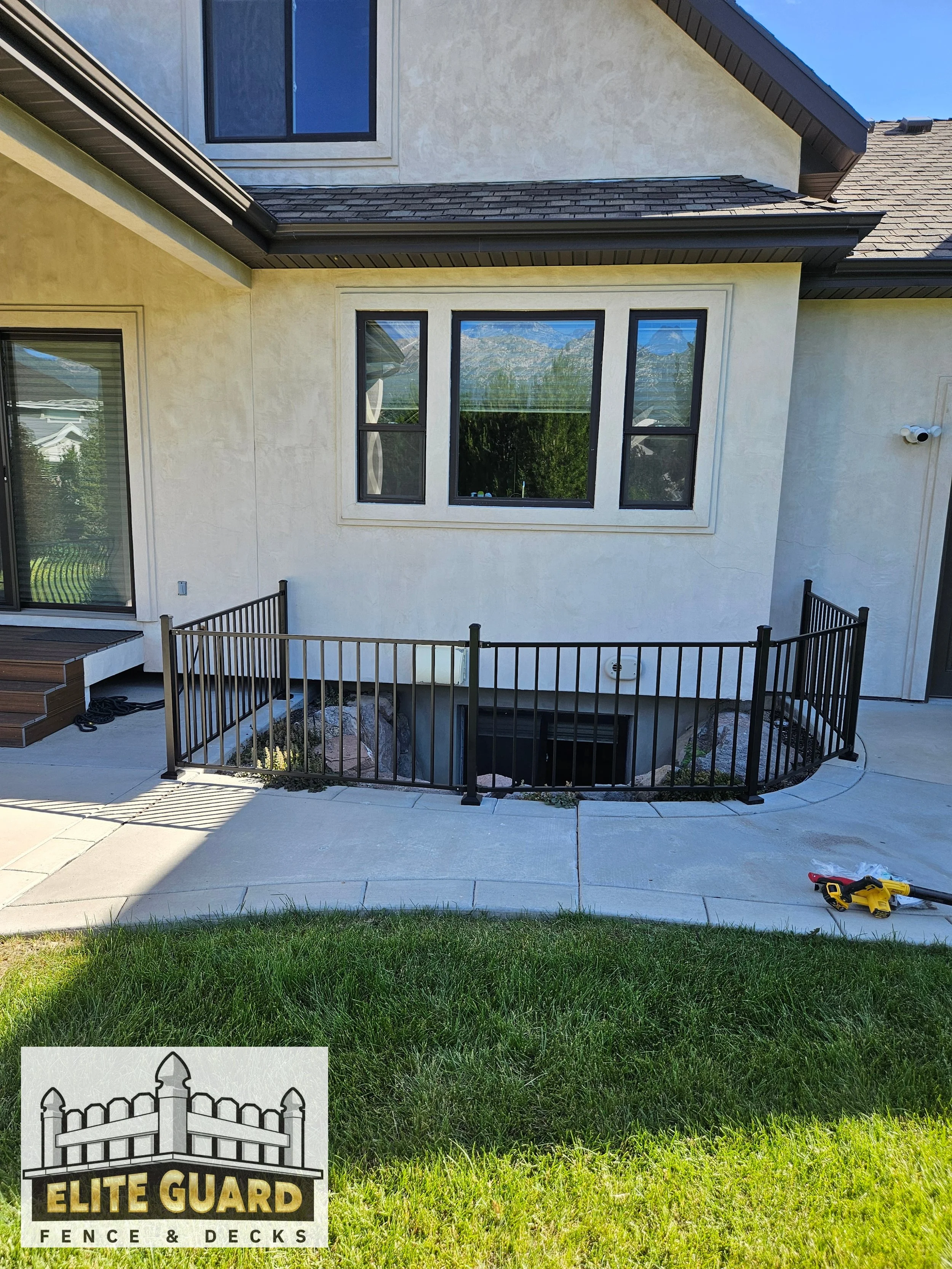 The image shows the back of a house with a small fenced-in area containing rocks and plants, a sliding glass door, a window above it, and a yellow power tool on the concrete patio in Payson, Utah.
