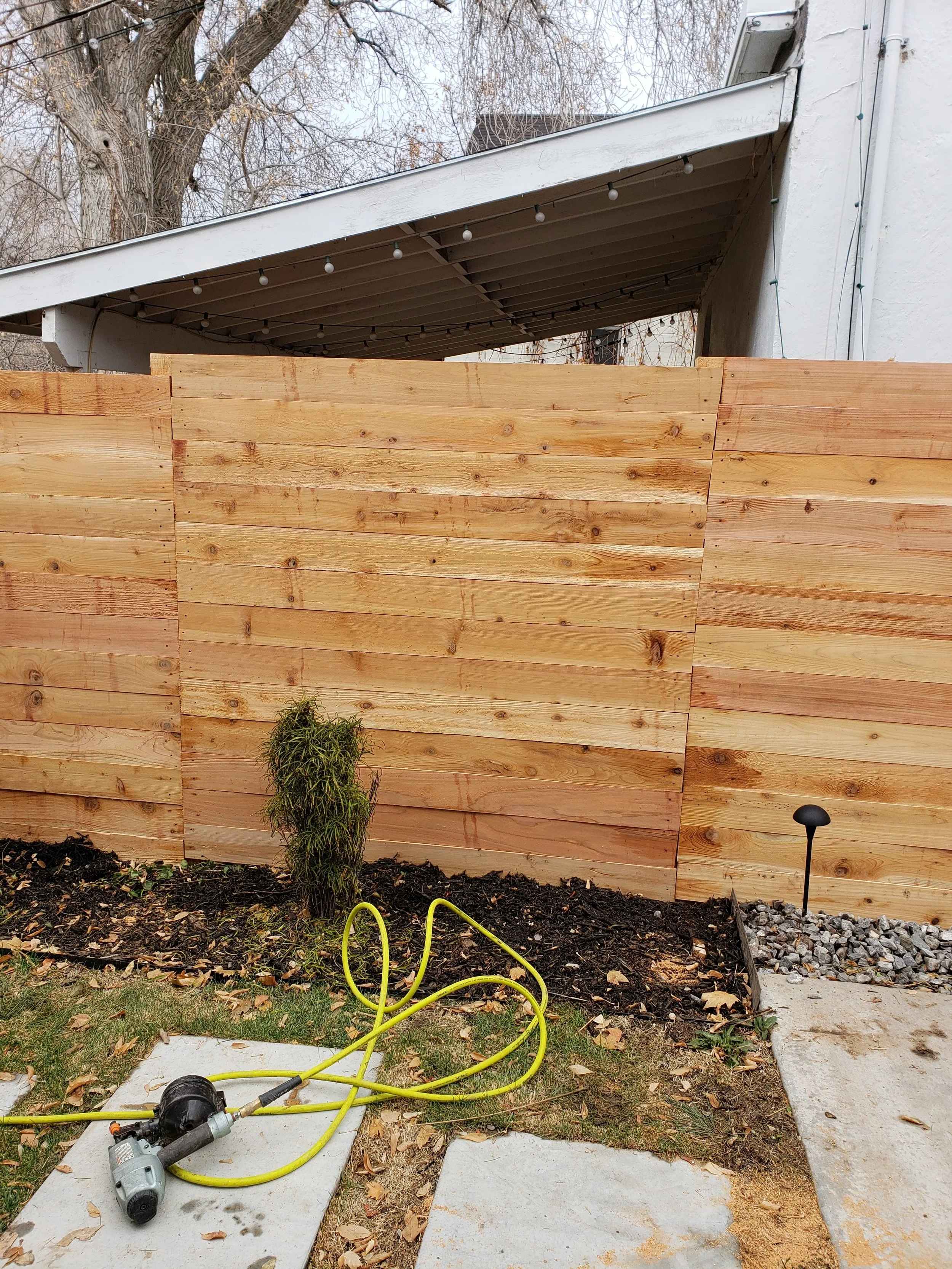 New wooden fence with planting bed and garden light, garden hose, and power tool on concrete pathway in Payson, UT .