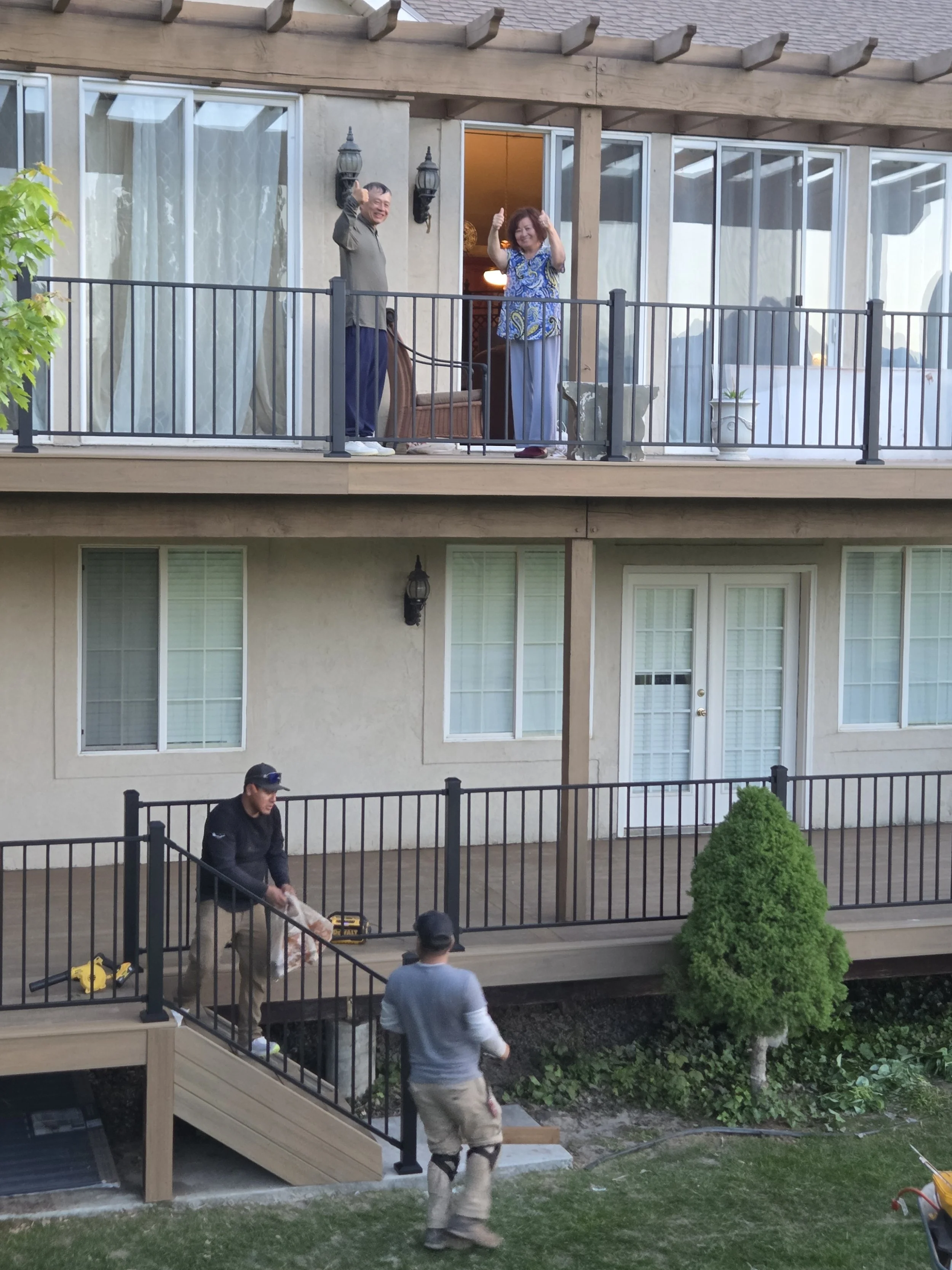 People standing on a second-story balcony waving at workers below who are installing or repairing the railing in Payson, Ut.