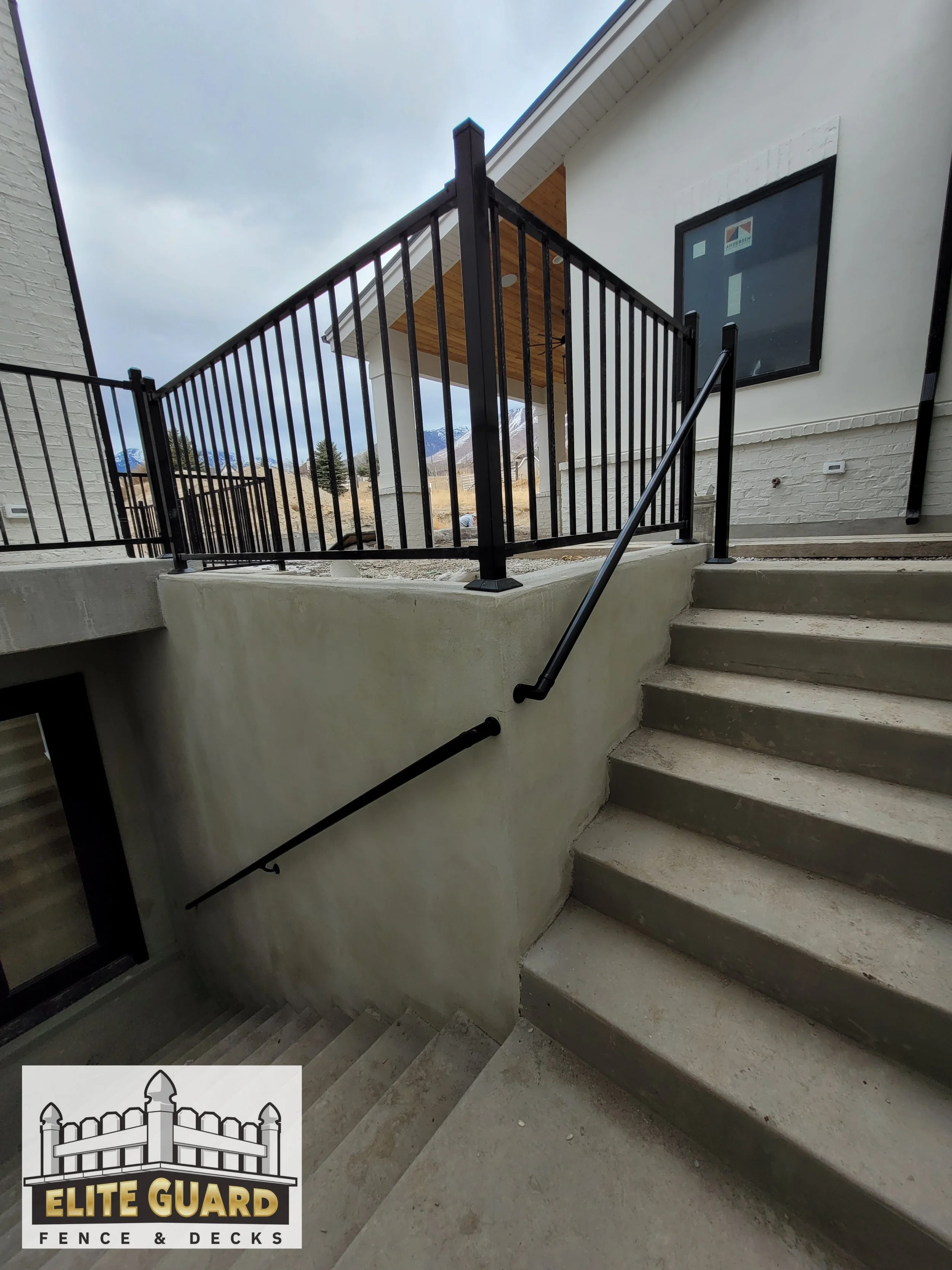 Outdoor stairs leading down to a basement entrance, with a black railing on top and a black handrail on the wall in Payson, Utah.