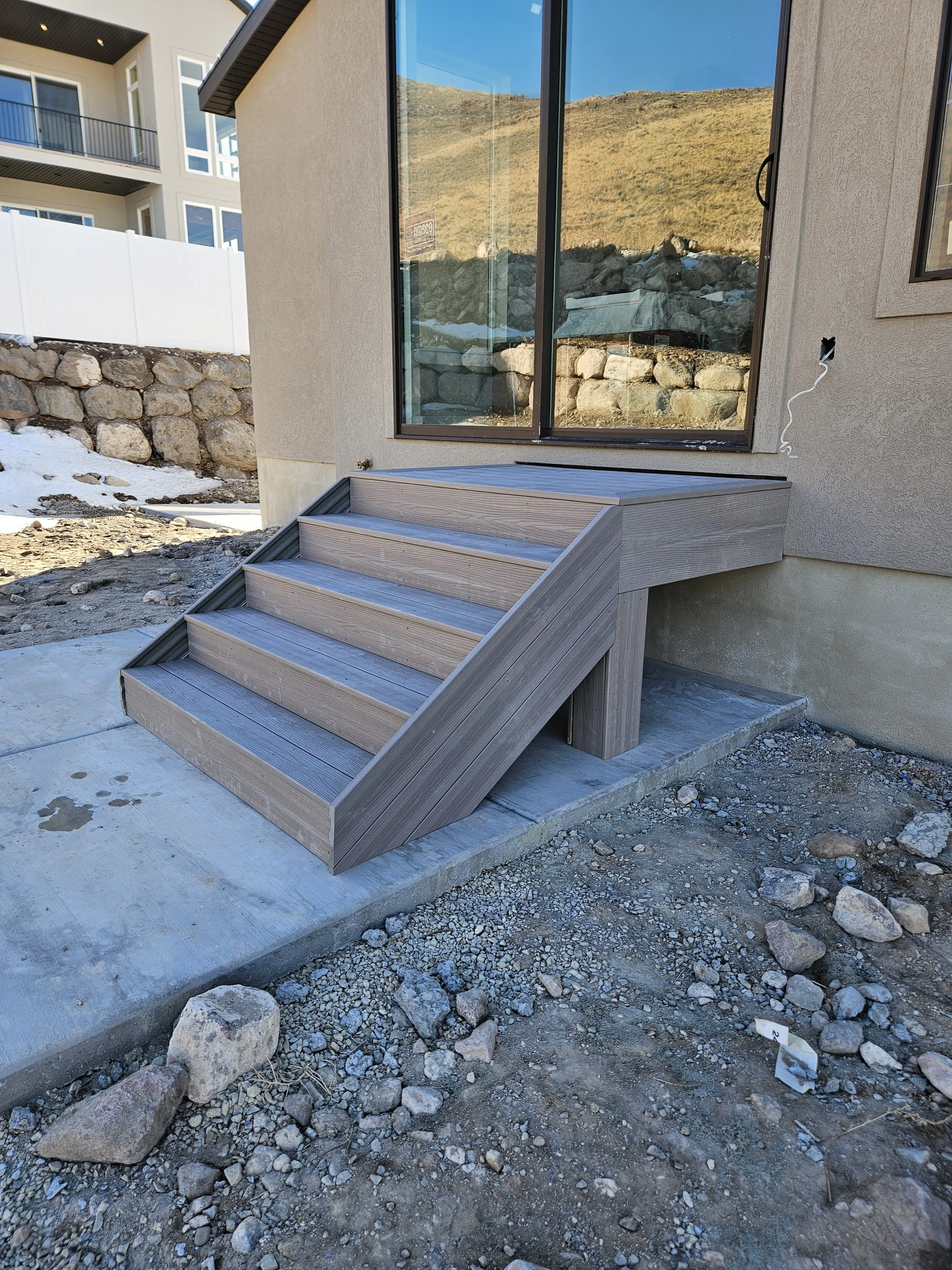 New wooden stairs leading up to a sliding glass door outside a house, with a rocky and dirt landscape around in Payson, UT.