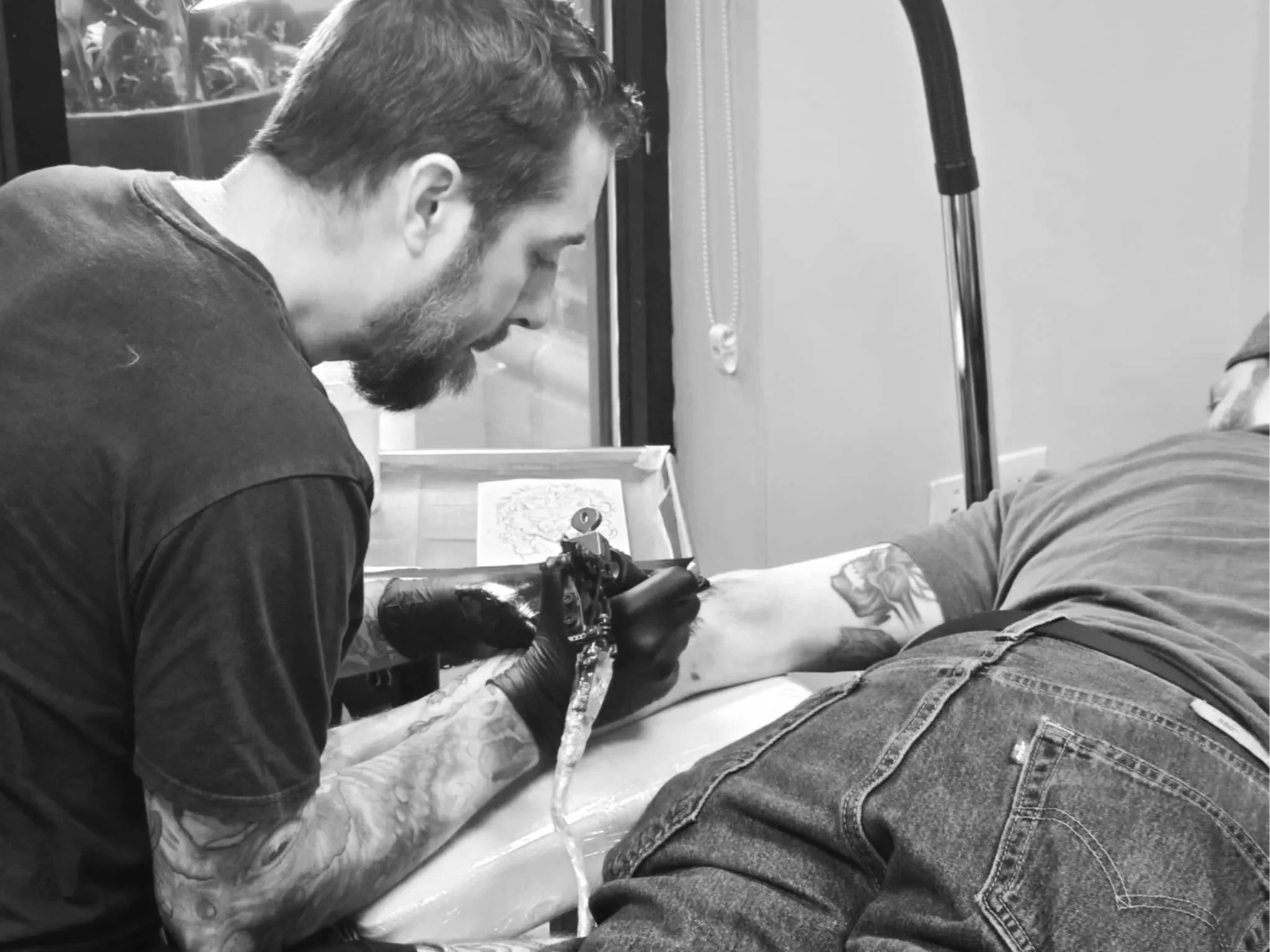 A tattoo artist tattooing a person's arm in a tattoo studio.