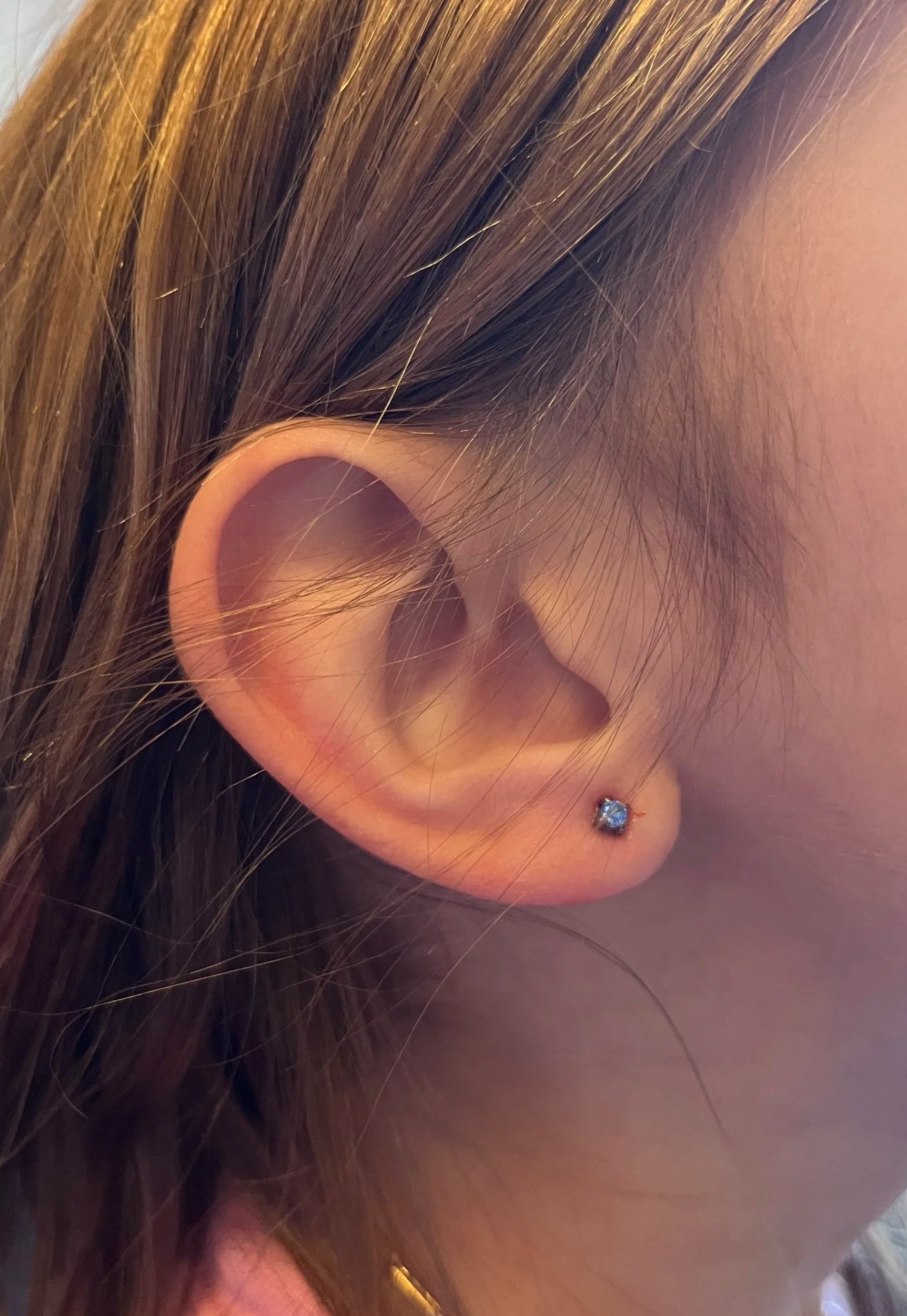 A close-up of a person's ear with a small stud earring and brown hair.