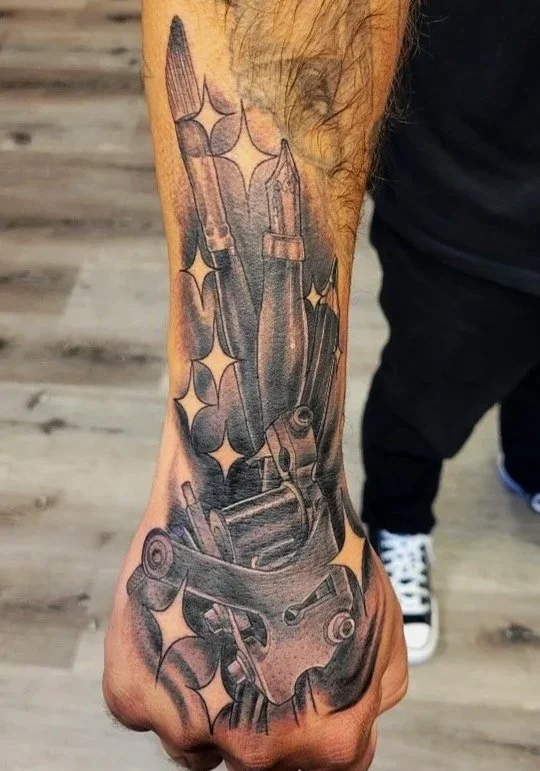 Tattoo of various screwdrivers and a mechanical tool on person’s forearm, with star-shaped sparkles around them.