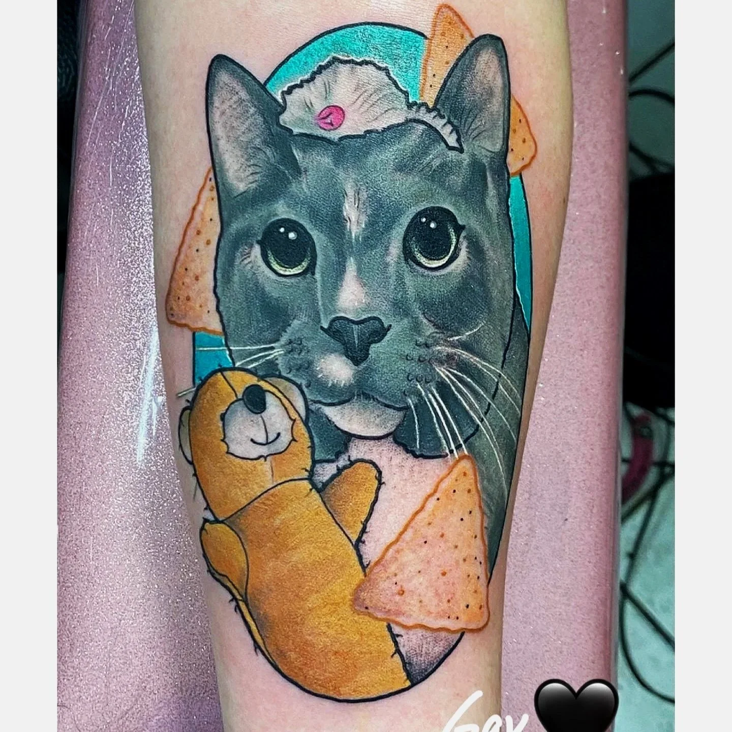 Tattoo of a realistic gray cat's face with large eyes, surrounded by illustration of a teddy bear, Doritos chips, and colorful background elements.