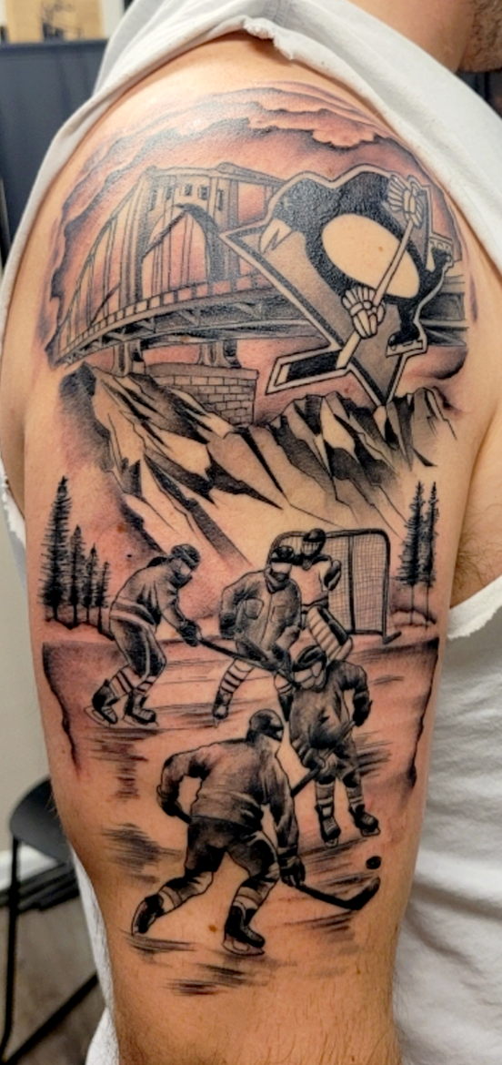 Black and gray tattoo featuring a mountain landscape with trees at the base, hockey players on ice, a bridge, and a large splash of clouds with a paint palette and artist's brush in the sky.