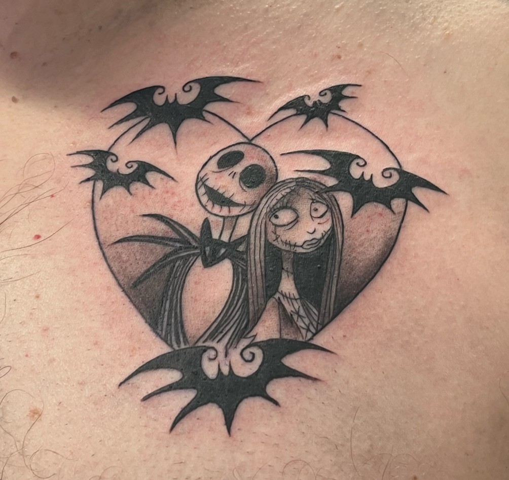 A tattoo of a heart contains characters from The Nightmare Before Christmas, including Jack Skellington and Sally, surrounded by bats.