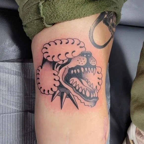 Tattoo of a fierce dog with sharp teeth and a chain around its neck on a person's thigh.