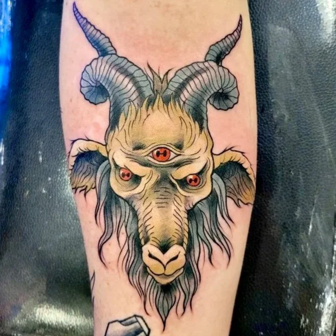 Tattoo of a goat's head with three eyes, large horns, and a beard, in a traditional style.
