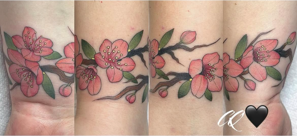 Tattoo of cherry blossoms with pink petals, green leaves, and dark brown branches across a person's side torso.