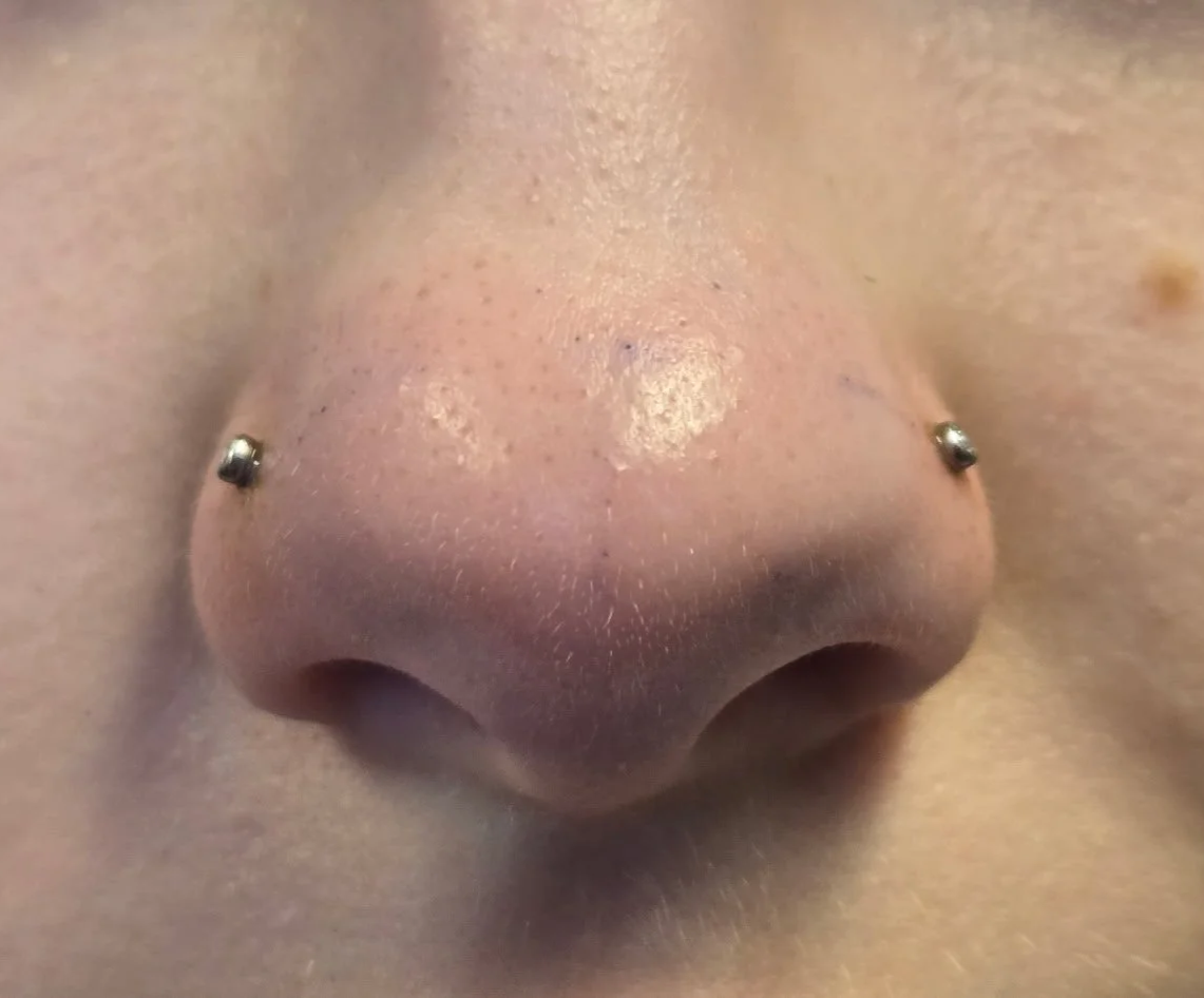 Close-up of a nose with two piercings and skin with visible pores.