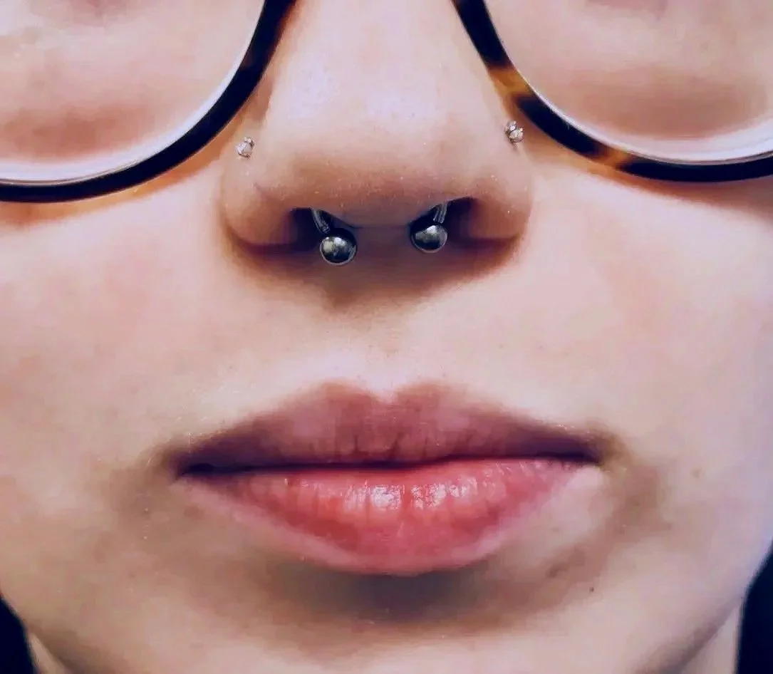 Close-up of a person with glasses and a nose ring, showing lips and part of the nose.
