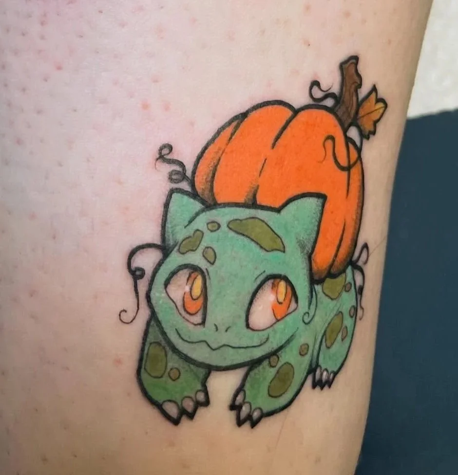 Colorful tattoo of a cute, cartoon-style chameleon with orange eyes, green spots, and a pumpkin on its back.