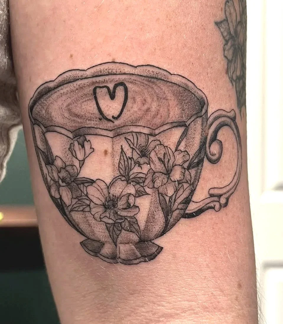 Tattoo of a teacup with floral design inside and a small heart symbol on the rim.