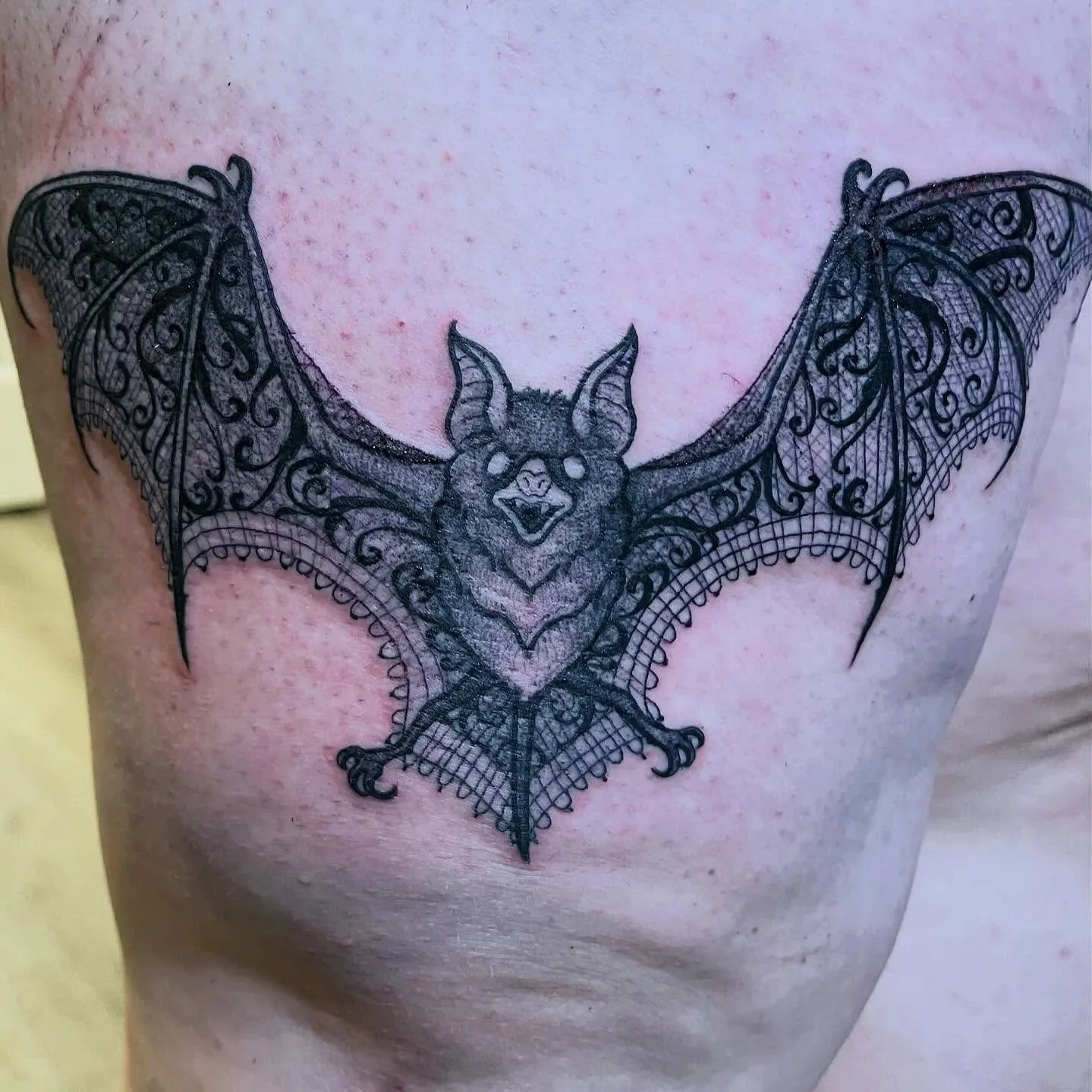 Tattoo of a bat with detailed, lacy wings on a person's upper chest.