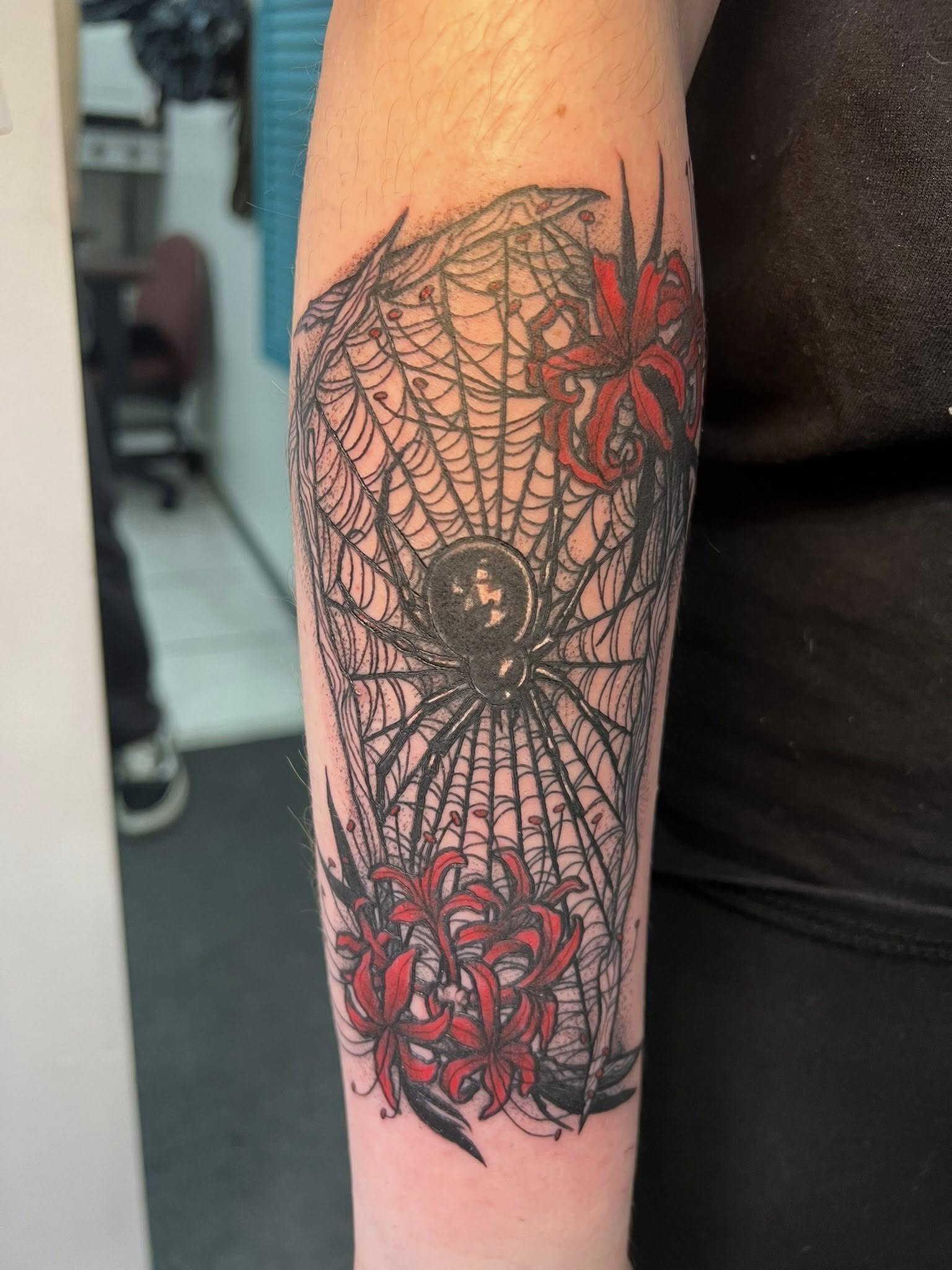 Tattoo of a spider in a web, adorned with red lilies on the arm.