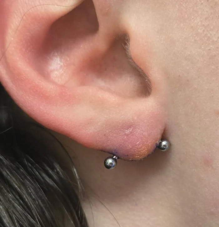Close-up of a person's ear with a small piercing at the earlobe, featuring a silver ball stud earring.
