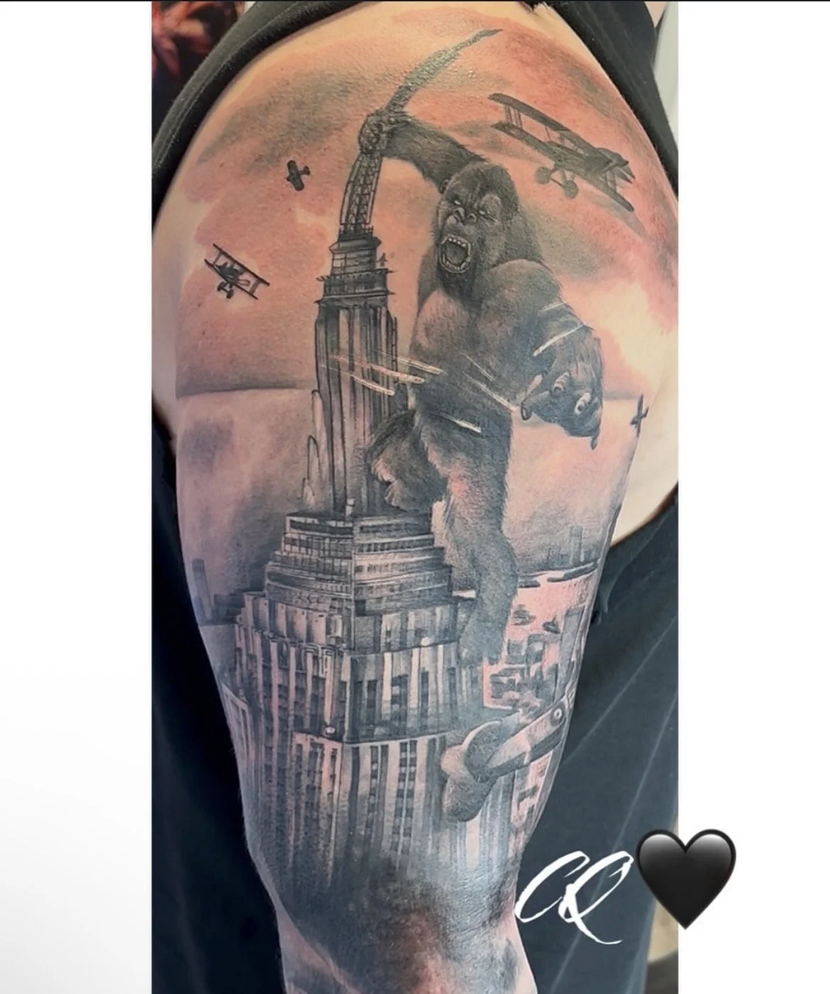 Tattoo of a giant gorilla roaring on top of a skyscraper under a sky with airplanes and a bird, with a black heart symbol and initials 'C&C' at the bottom.