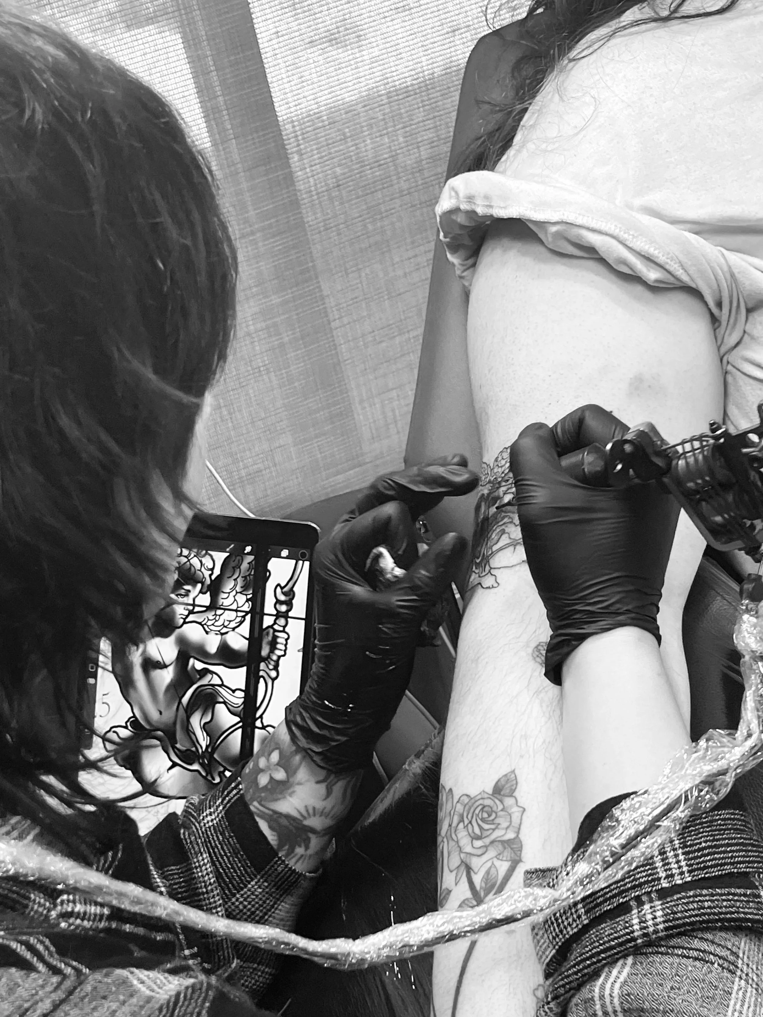 A person with tattoos on their arm getting a tattoo on their upper arm from an artist wearing black gloves in a tattoo studio.